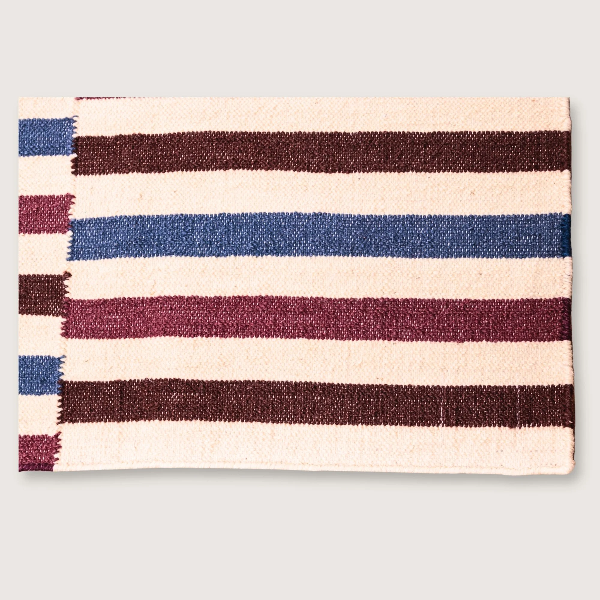 Saanjh handwoven wool rug with striped design in muted reds, deep browns and calm blues on a natural ivory base, woven by artisans in India.