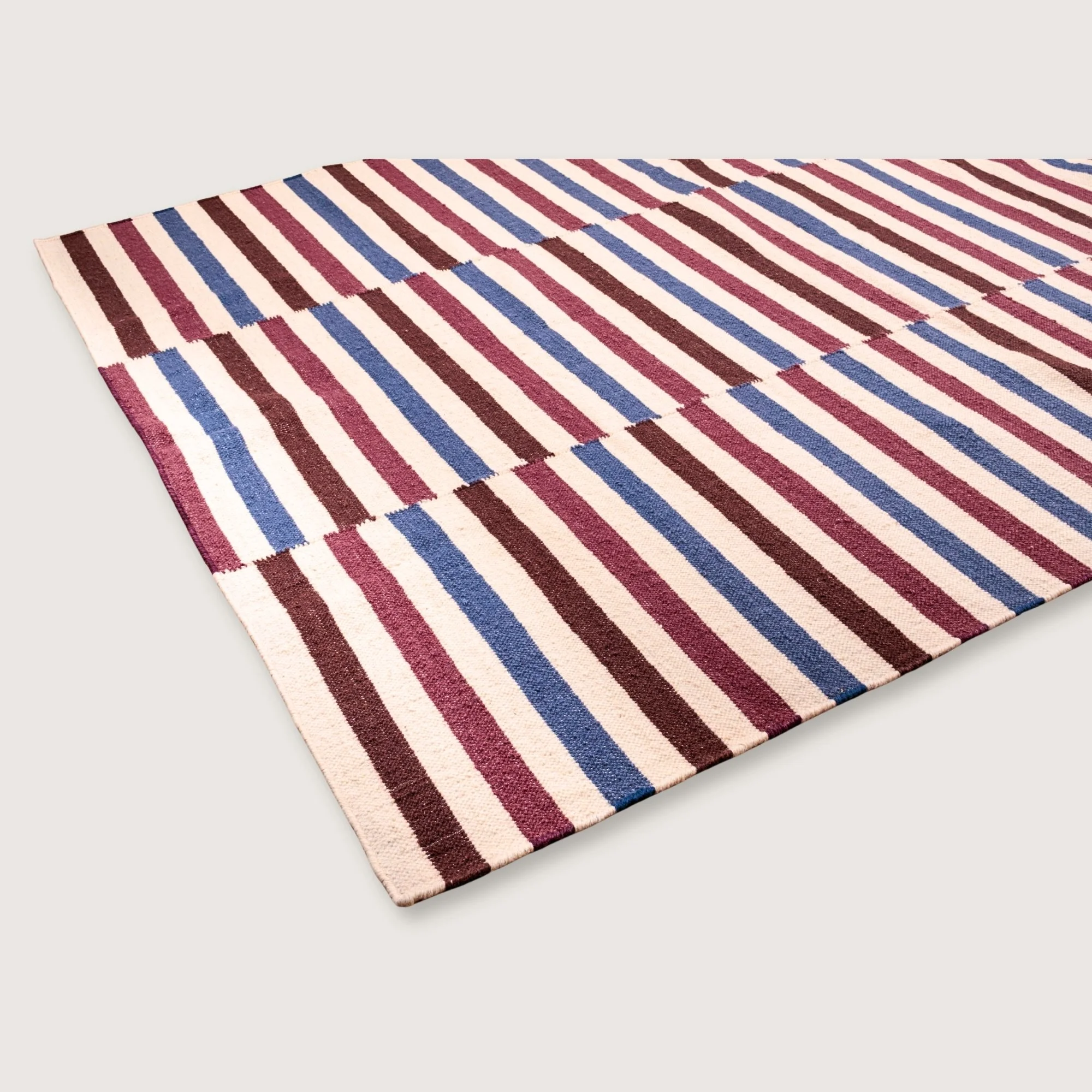 Saanjh handwoven wool rug with striped design in muted reds, deep browns and calm blues on a natural ivory base, woven by artisans in India.