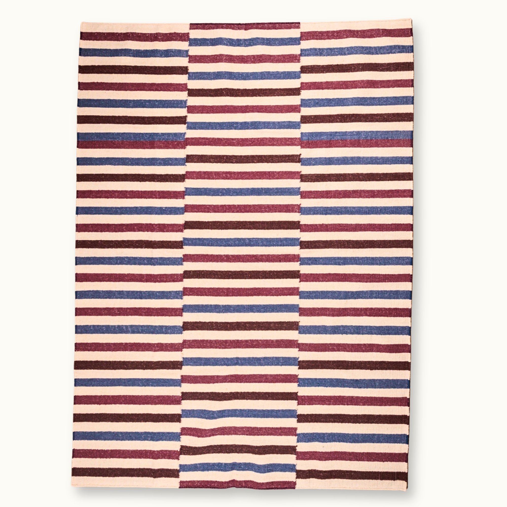Saanjh handwoven wool rug with striped design in muted reds, deep browns and calm blues on a natural ivory base, woven by artisans in India.