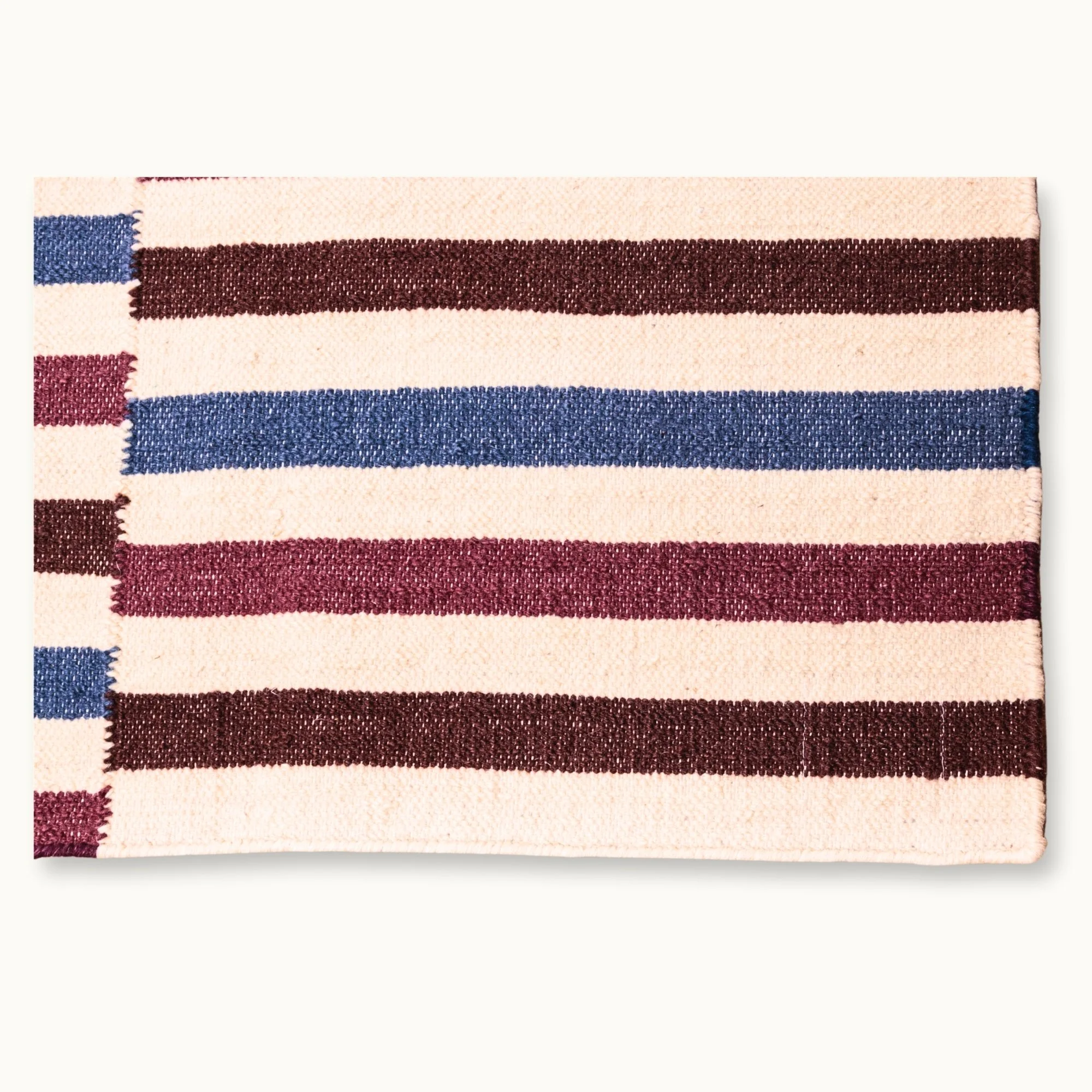 Saanjh handwoven wool rug with striped design in muted reds, deep browns and calm blues on a natural ivory base, woven by artisans in India.