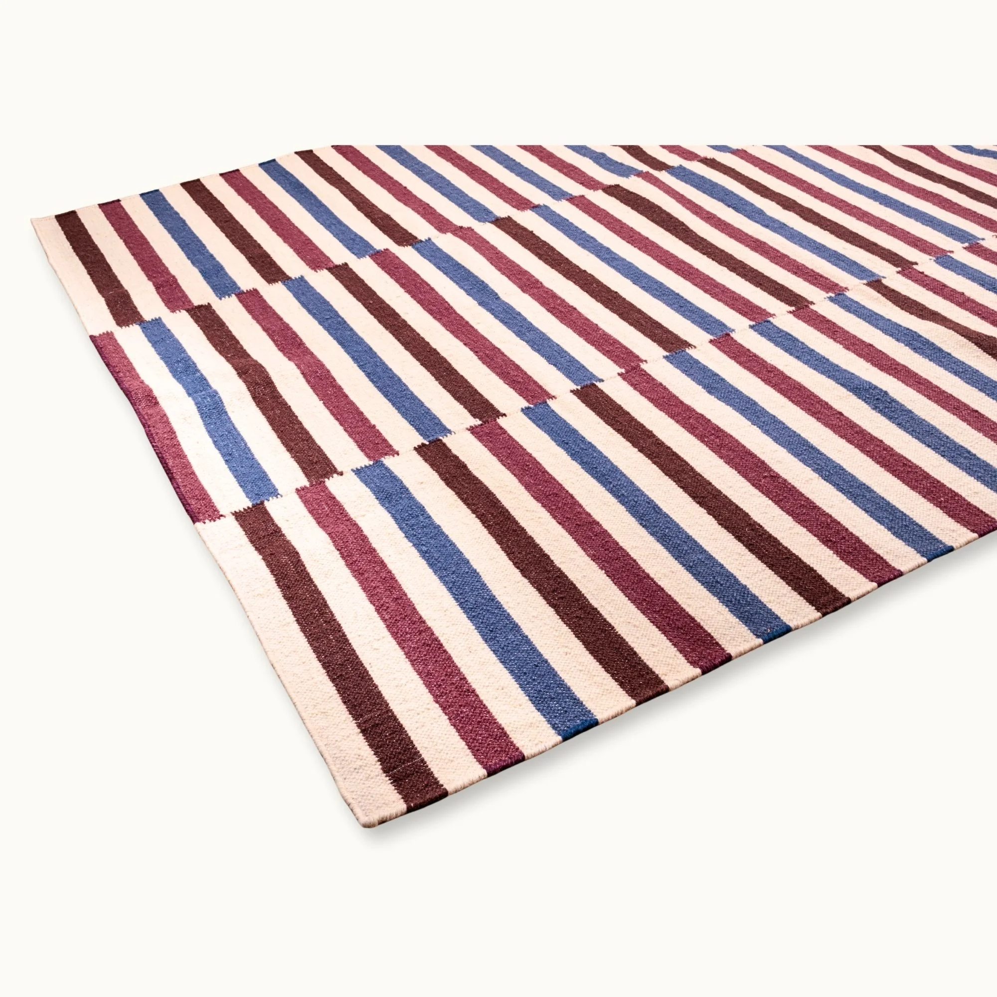 Saanjh handwoven wool rug with striped design in muted reds, deep browns and calm blues on a natural ivory base, woven by artisans in India.