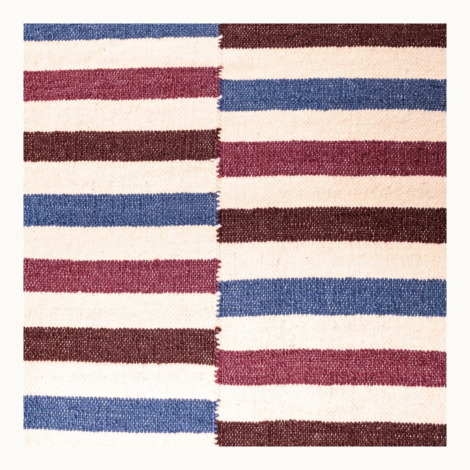 Saanjh handwoven wool rug with striped design in muted reds, deep browns and calm blues on a natural ivory base, woven by artisans in India.