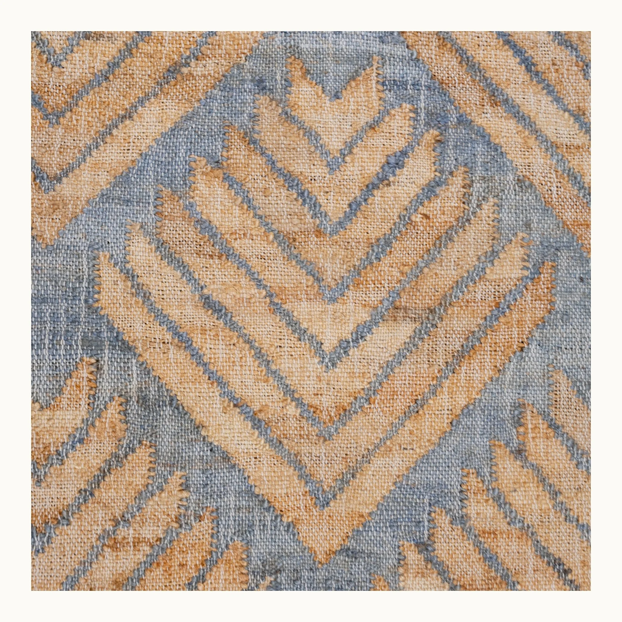 Handgeweven jute loper met een platgeweven structuur en een geometrisch patroon geïnspireerd op palmbladeren, uitgevoerd in gedempte blauwe en natuurlijke zandtinten.