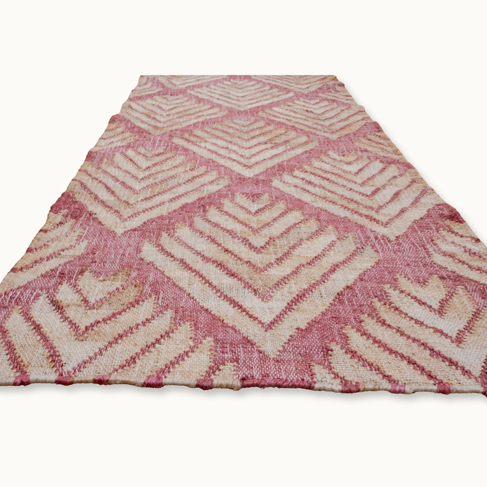 Handgeweven jute loper met een platgeweven structuur en een geometrisch patroon geïnspireerd op palmbladeren, uitgevoerd in zachtroze en natuurlijke zandtinten.