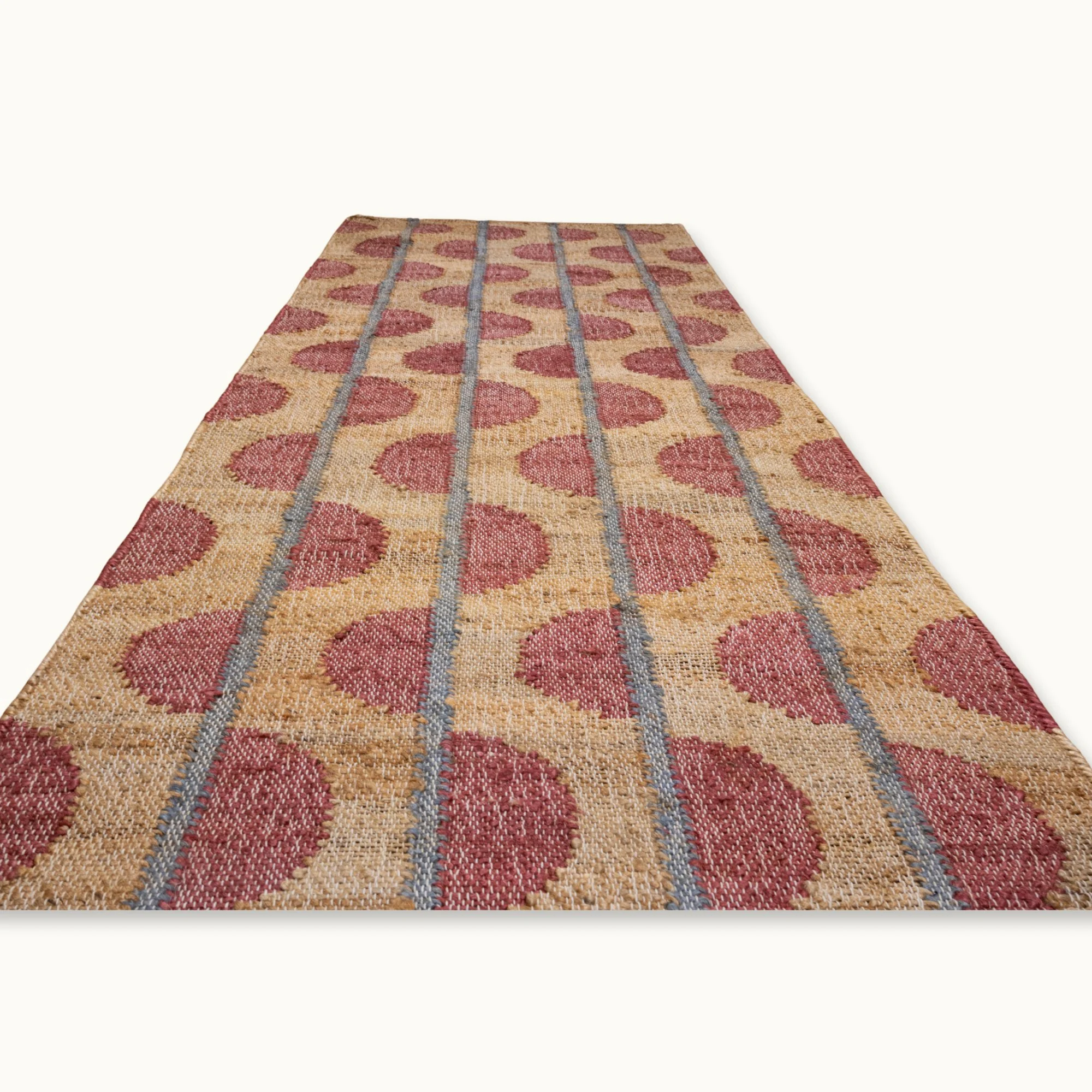 Handwoven jute rug with repeating half-moon pattern in dusty pink and natural sand tones.