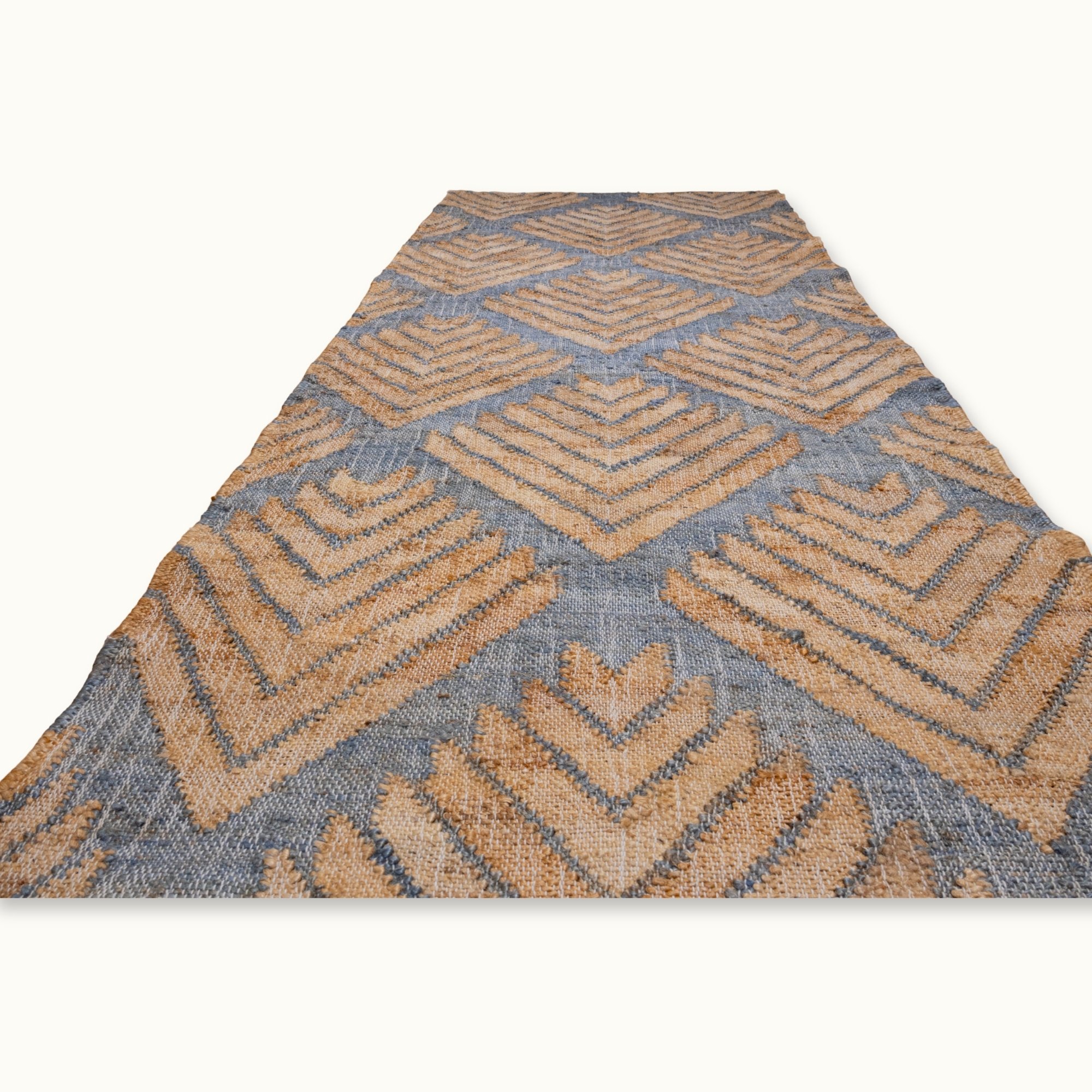 Handgeweven jute loper met een platgeweven structuur en een geometrisch patroon geïnspireerd op palmbladeren, uitgevoerd in gedempte blauwe en natuurlijke zandtinten.