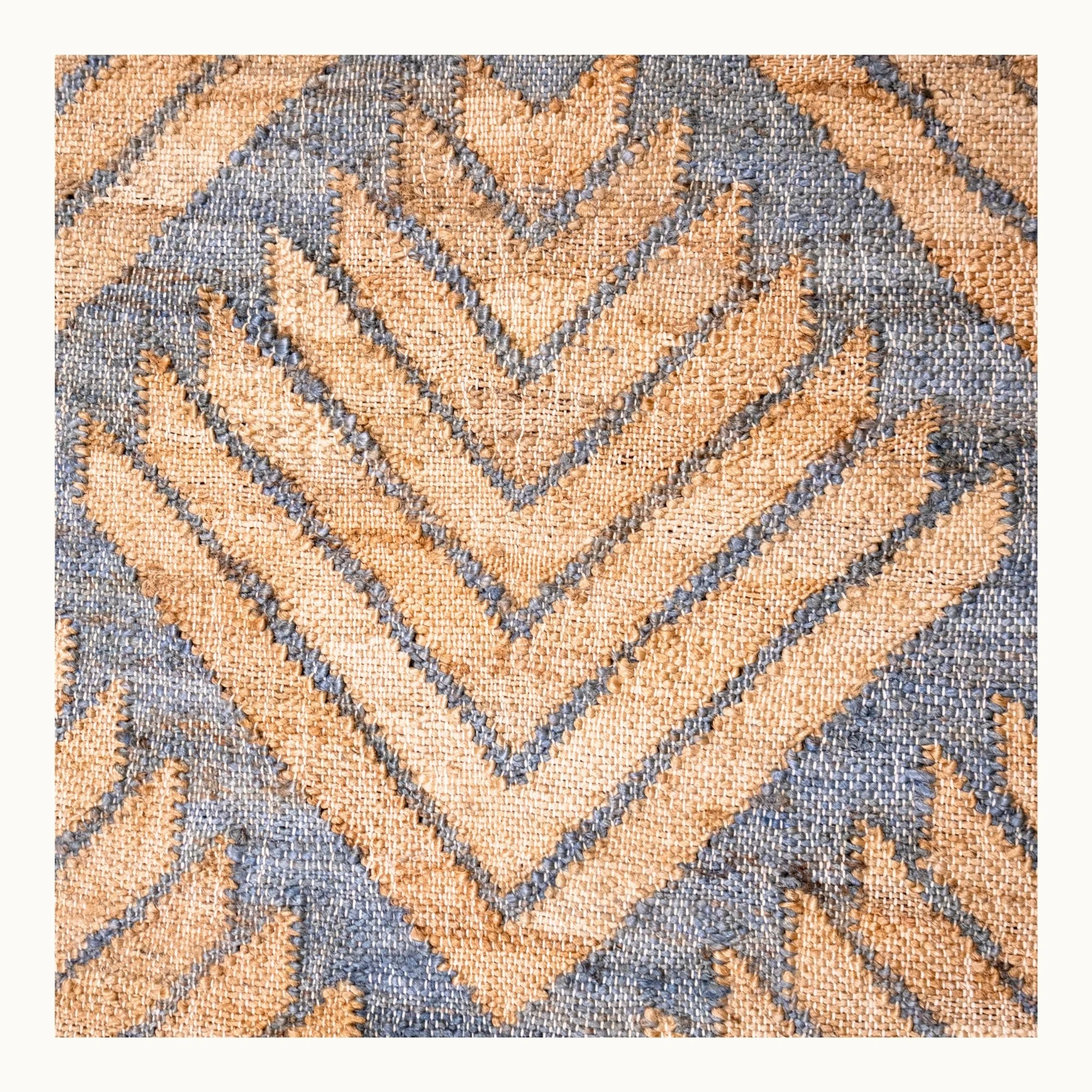 Handgeweven jute vloerkleed met een getextureerd, op palmen geïnspireerd geometrisch patroon in natuurlijke zand- en gedempte blauwgrijze tinten.