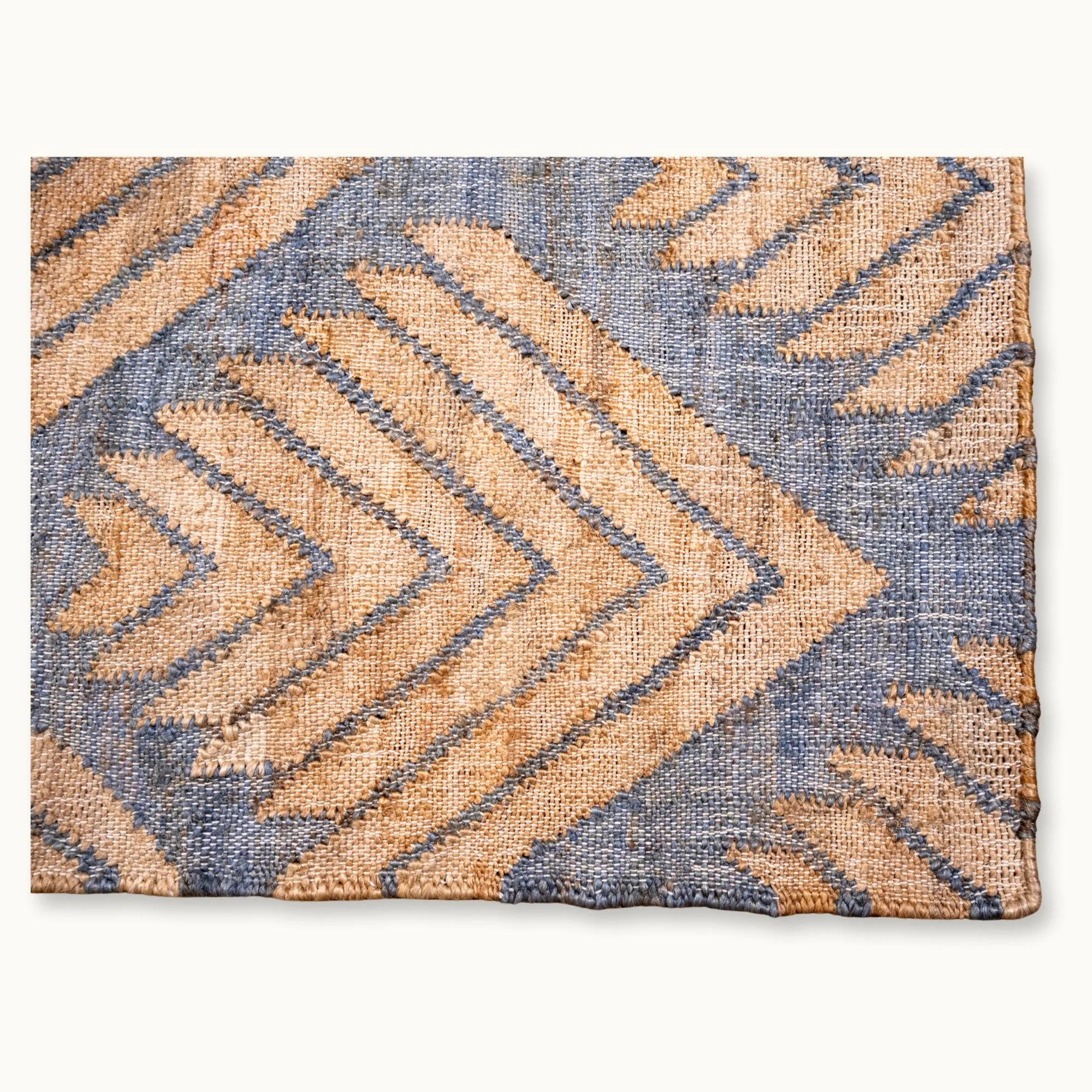 Handgeweven jute vloerkleed met een getextureerd, op palmen geïnspireerd geometrisch patroon in natuurlijke zand- en gedempte blauwgrijze tinten.