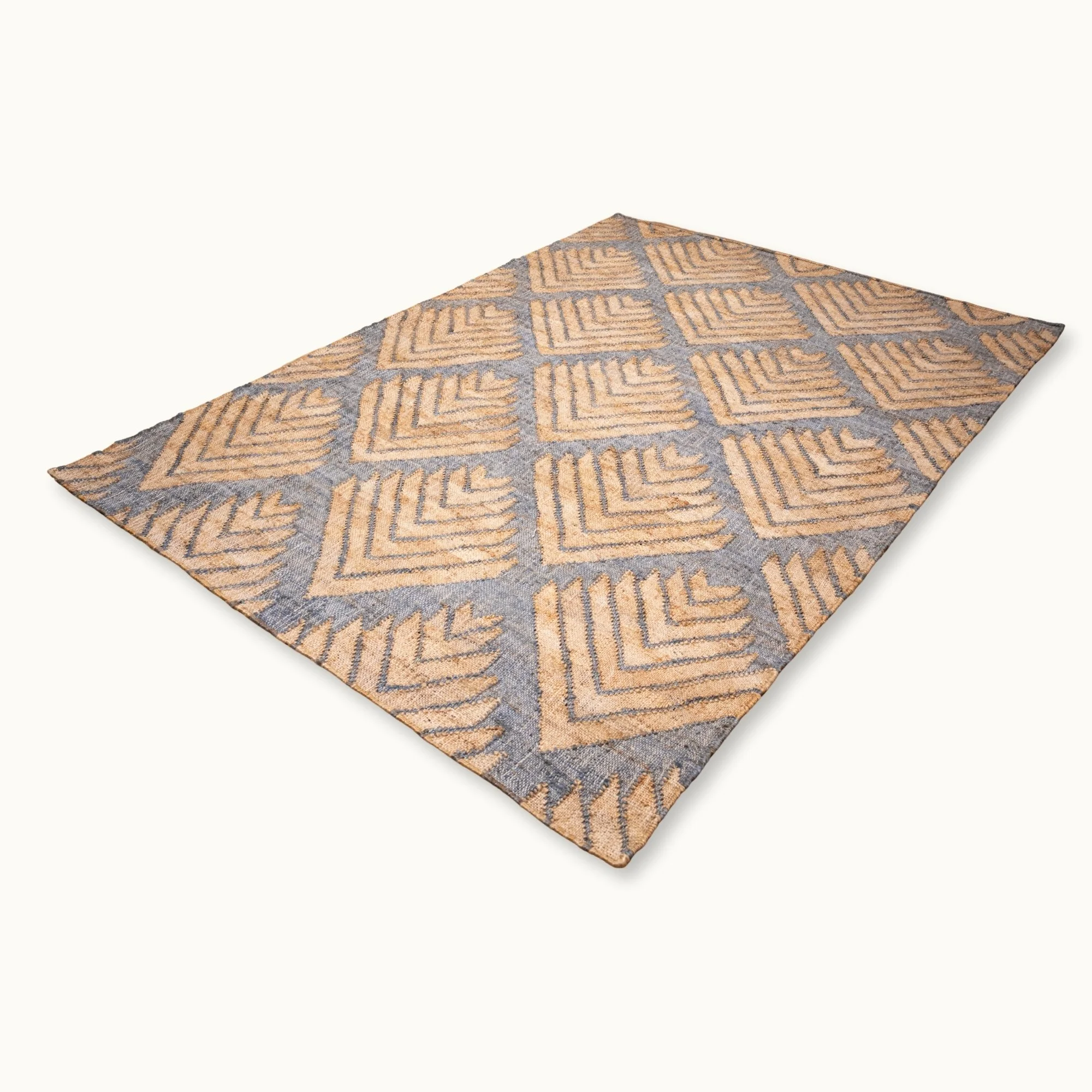 Handgeweven jute vloerkleed met een getextureerd, op palmen geïnspireerd geometrisch patroon in natuurlijke zand- en gedempte blauwgrijze tinten.