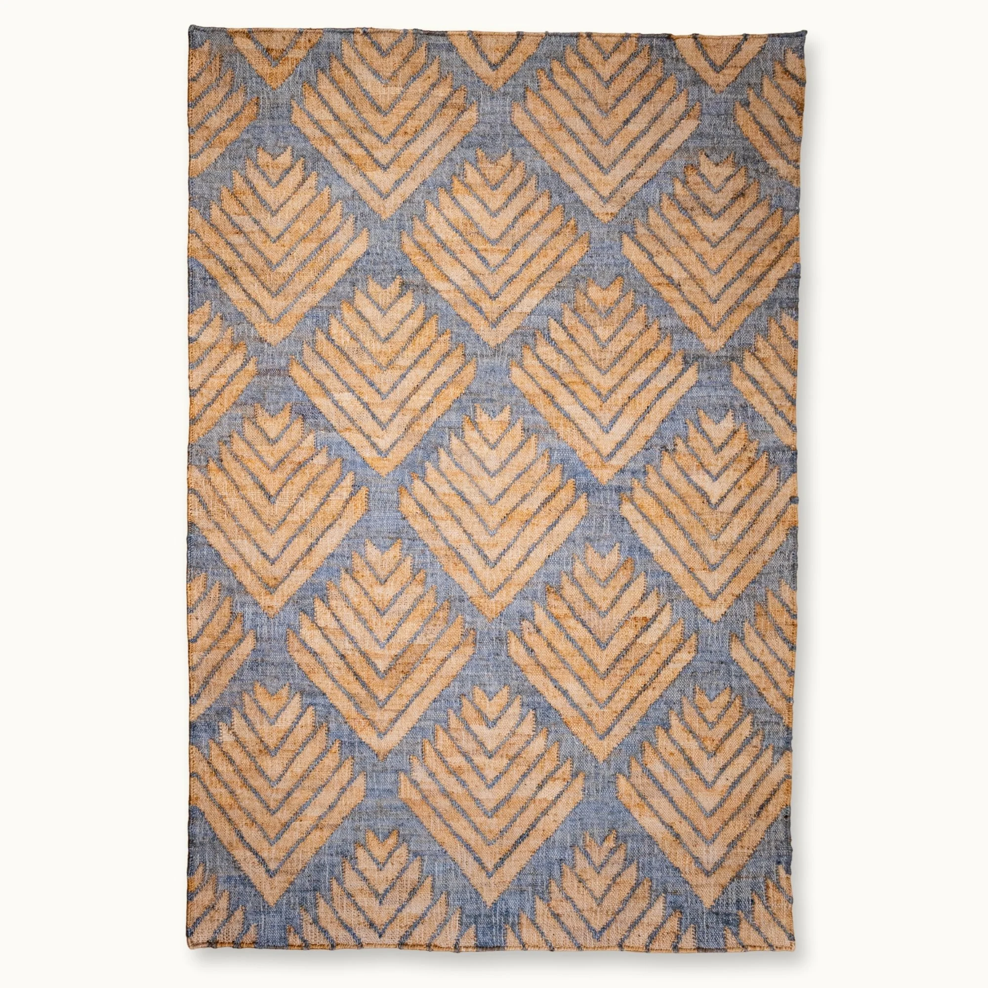 Handgeweven jute vloerkleed met een getextureerd, op palmen geïnspireerd geometrisch patroon in natuurlijke zand- en gedempte blauwgrijze tinten.