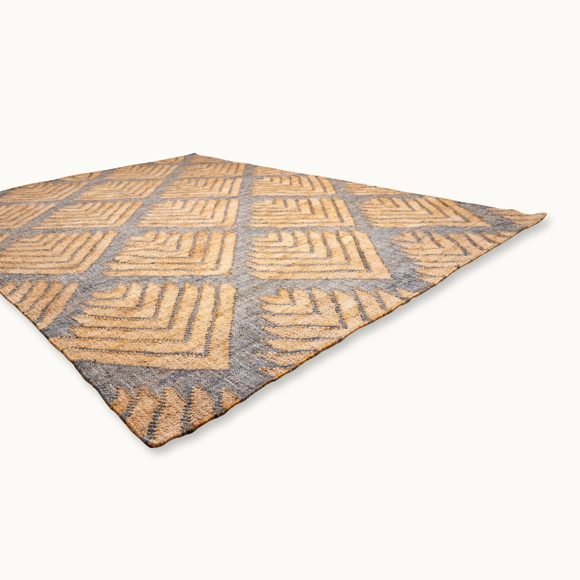 Handgeweven jute vloerkleed met een getextureerd, op palmen geïnspireerd geometrisch patroon in natuurlijke zand- en gedempte blauwgrijze tinten.