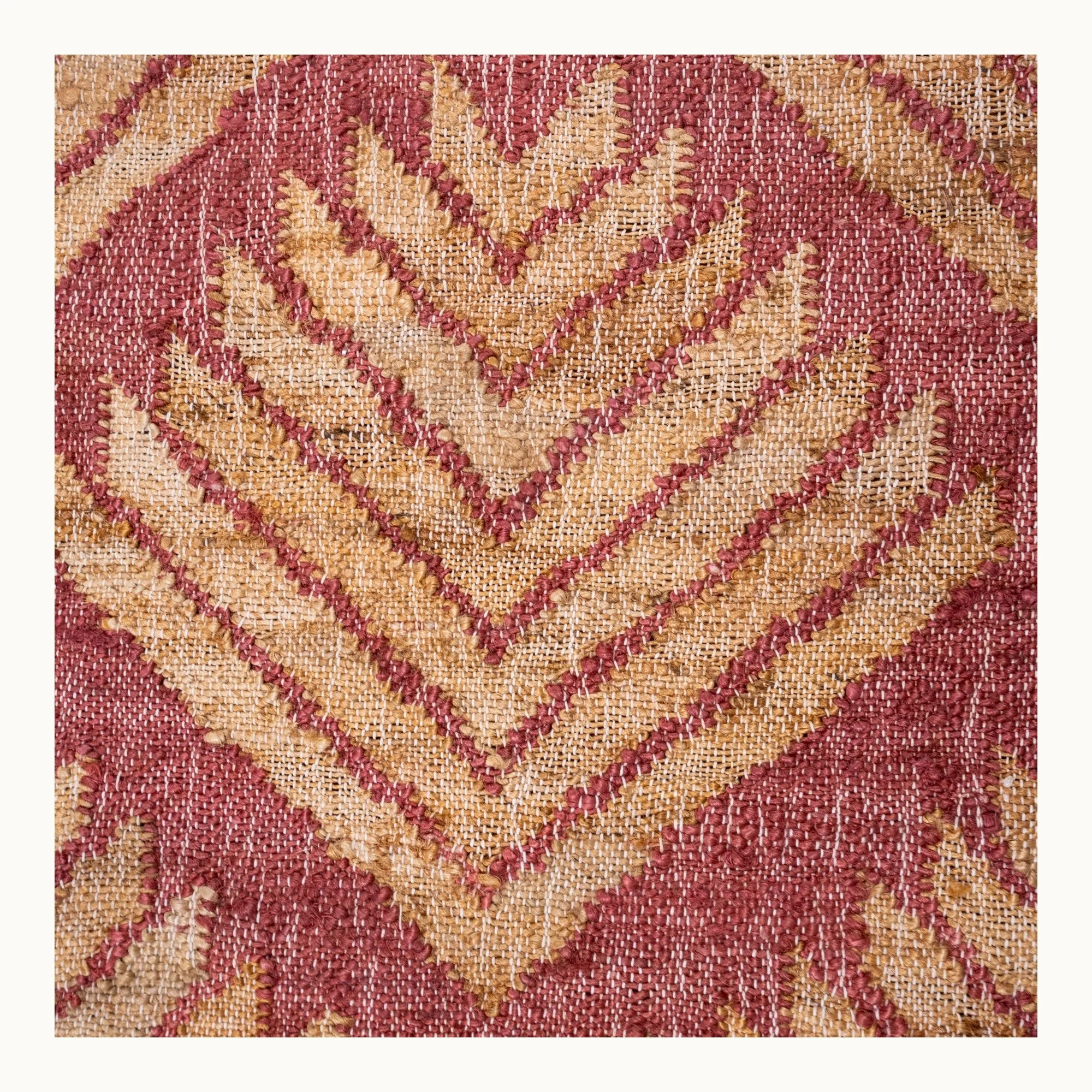 Handgeweven jute vloerkleed met een gestructureerd, op palmbladeren geïnspireerd geometrisch patroon in oudroze en natuurlijke zandtinten.