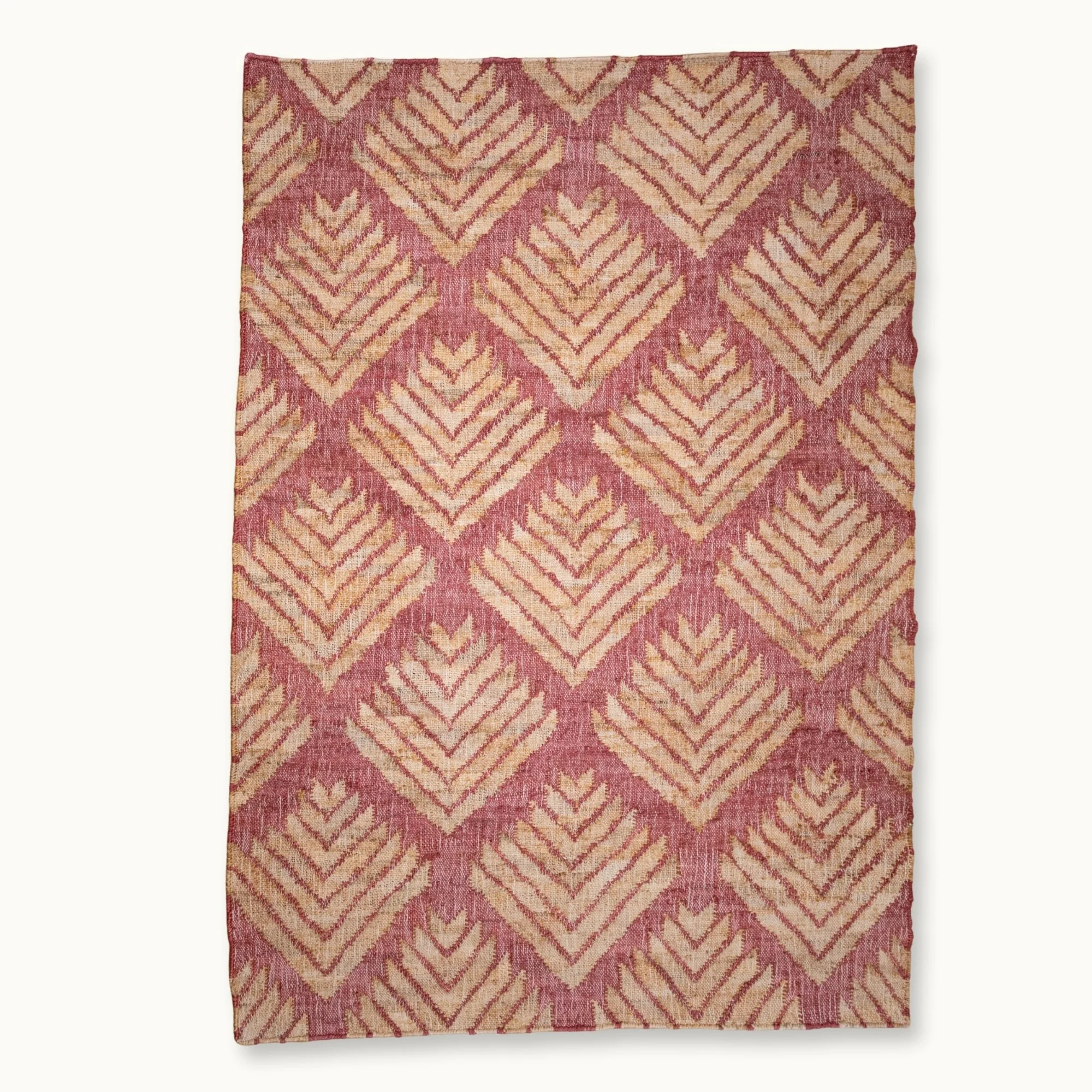 Handgeweven jute vloerkleed met een gestructureerd, op palmbladeren geïnspireerd geometrisch patroon in oudroze en natuurlijke zandtinten.