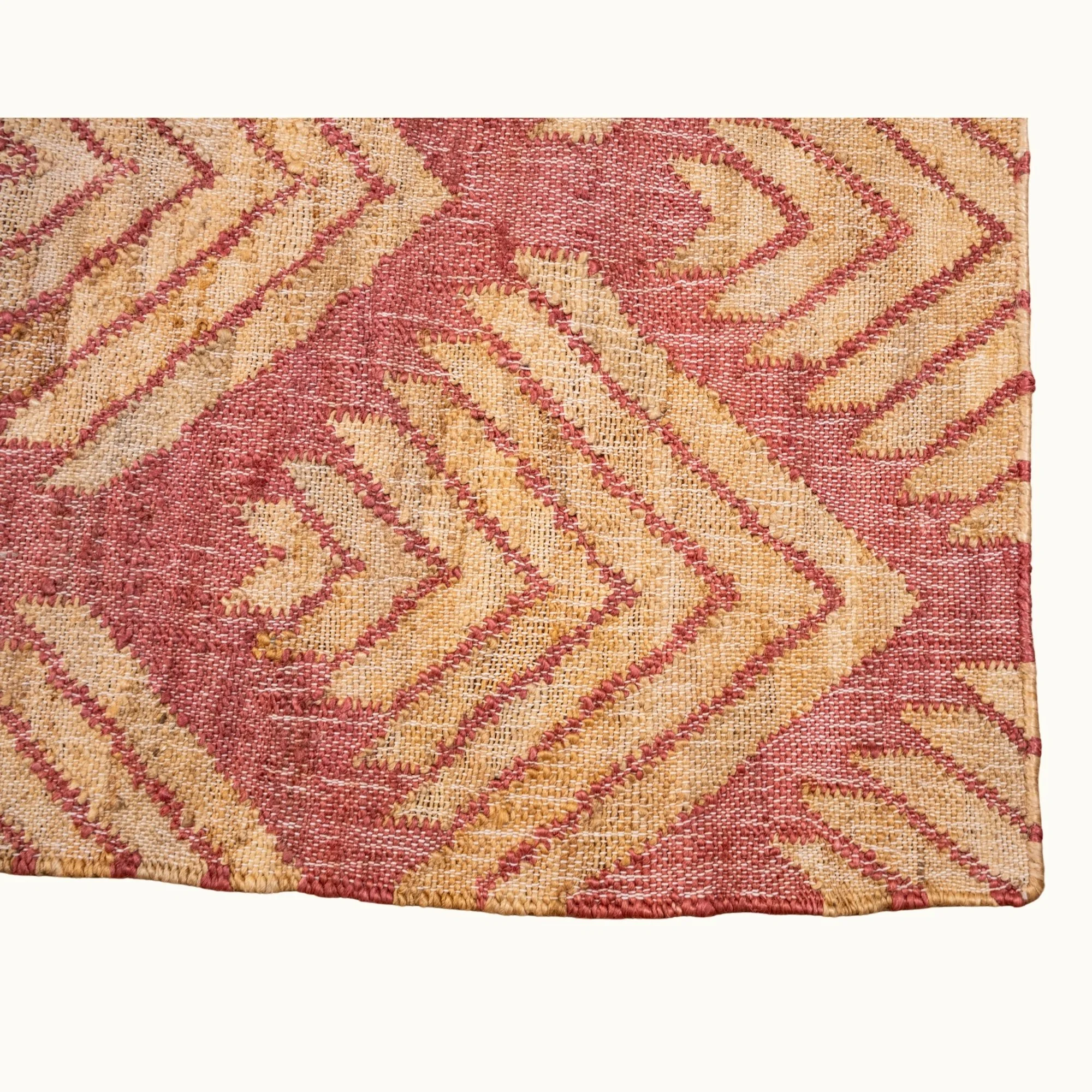 Handgeweven jute vloerkleed met een gestructureerd, op palmbladeren geïnspireerd geometrisch patroon in oudroze en natuurlijke zandtinten.