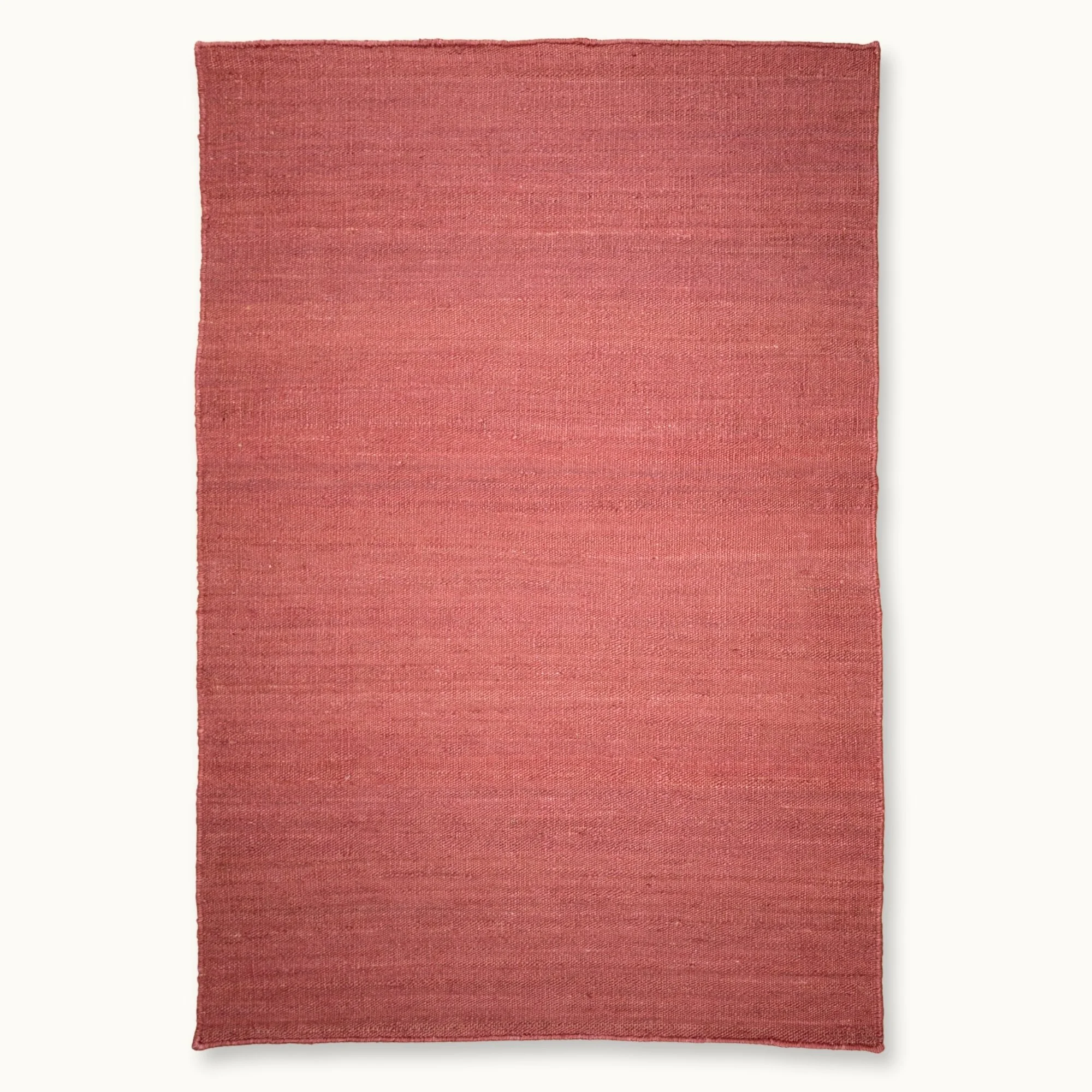 Een eenvoudig, handgeweven jute vloerkleed in zachte, oudroze tinten met een subtiele natuurlijke structuur.