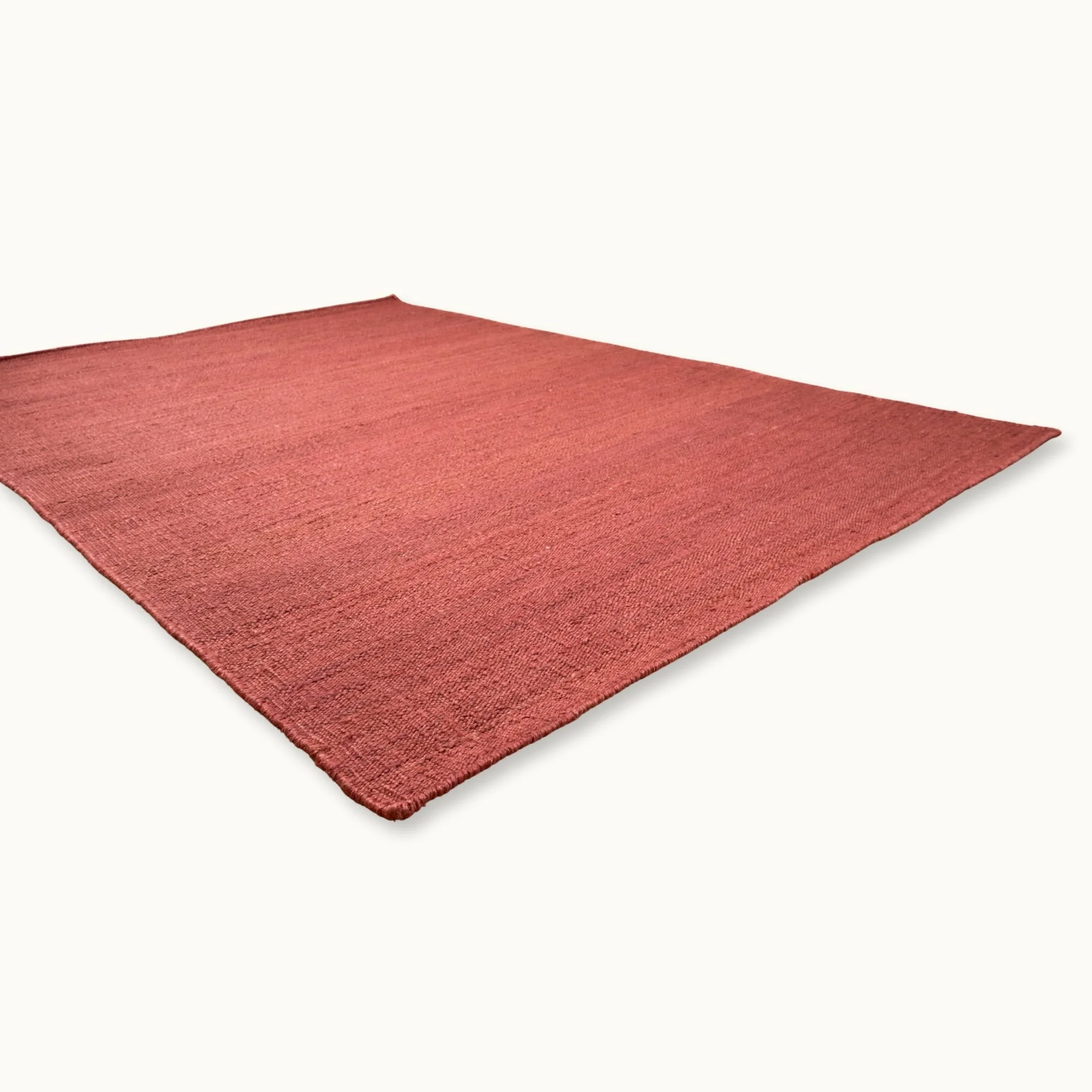 Een eenvoudig, handgeweven jute vloerkleed in zachte, oudroze tinten met een subtiele natuurlijke structuur.