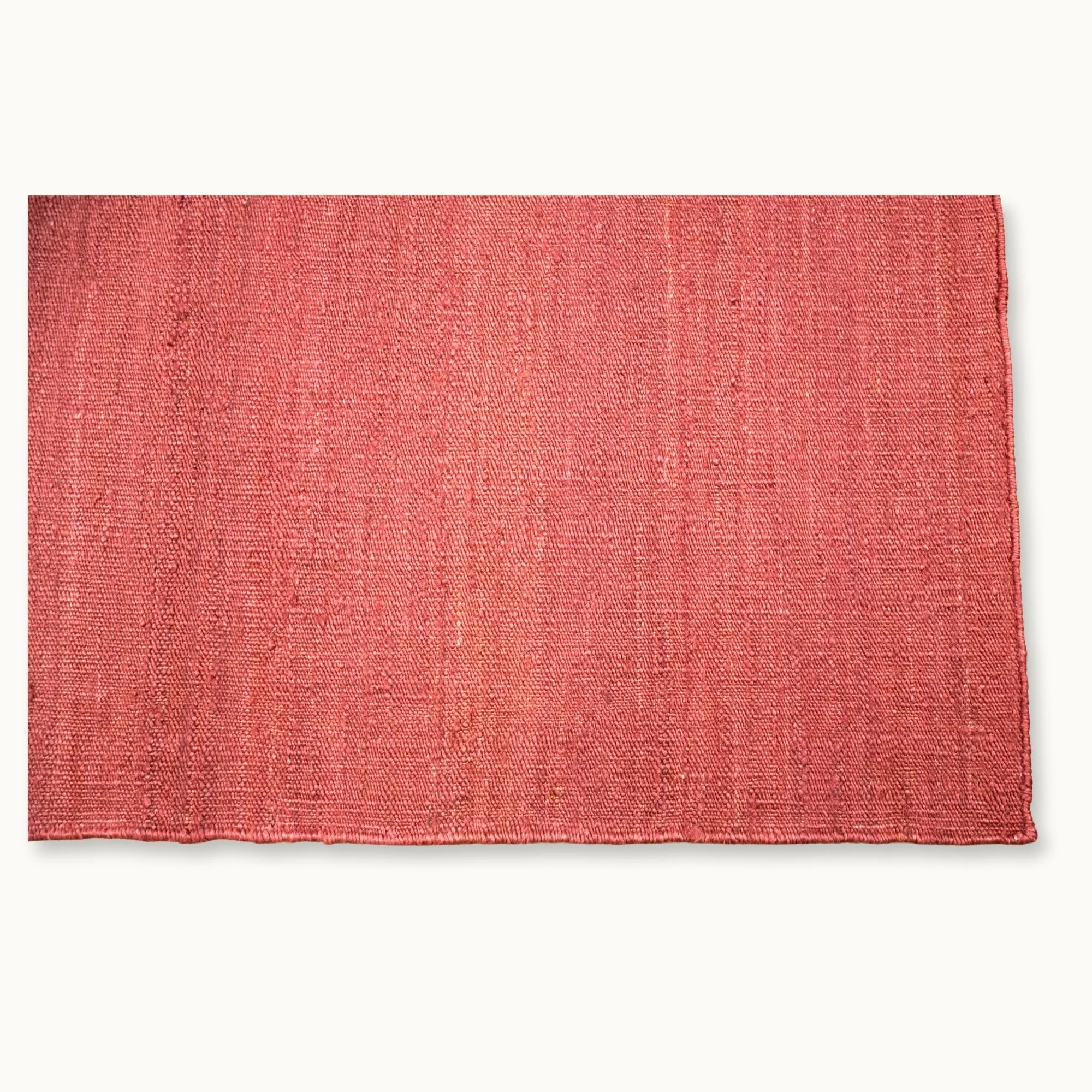 Een eenvoudig, handgeweven jute vloerkleed in zachte, oudroze tinten met een subtiele natuurlijke structuur.
