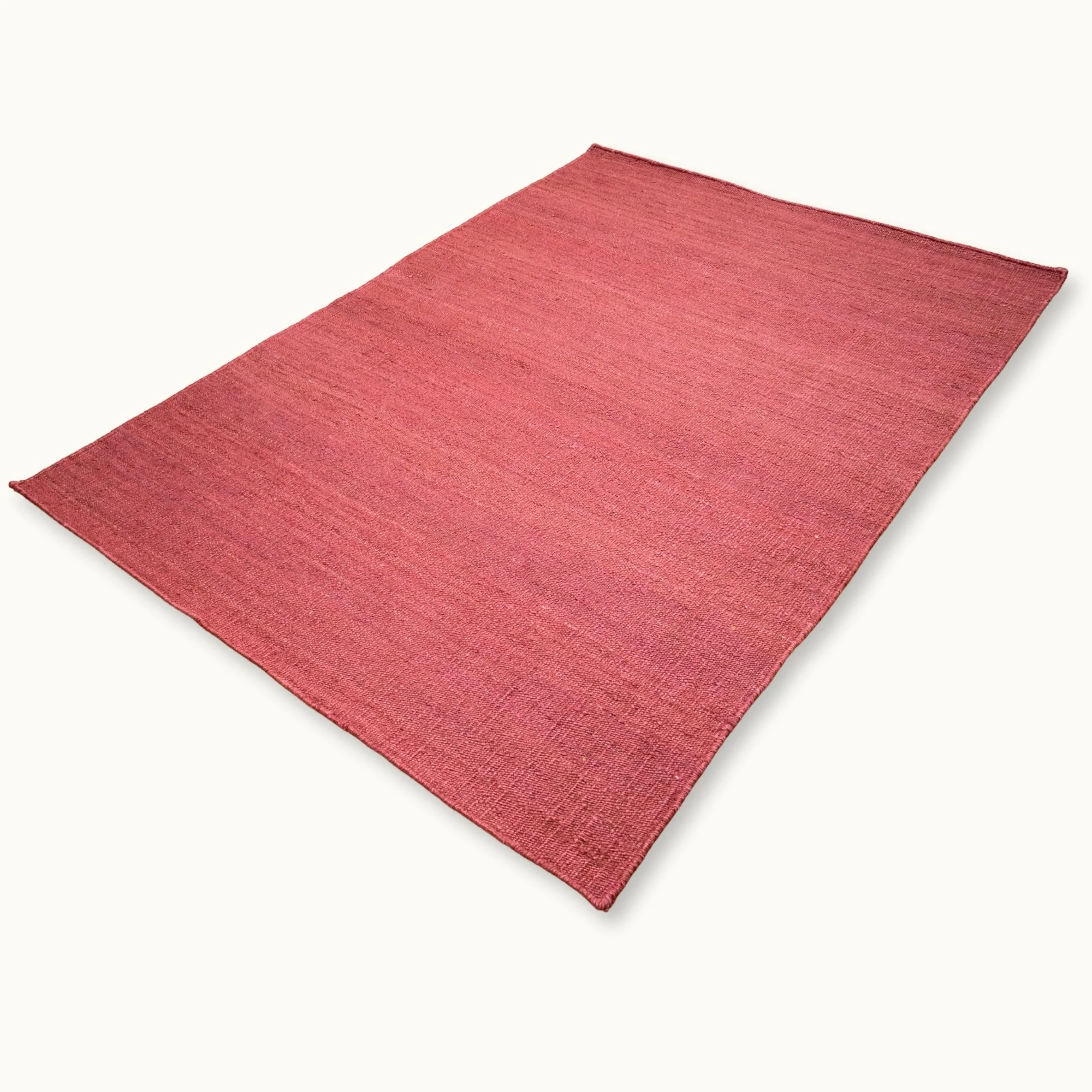 Een eenvoudig, handgeweven jute vloerkleed in zachte, oudroze tinten met een subtiele natuurlijke structuur.