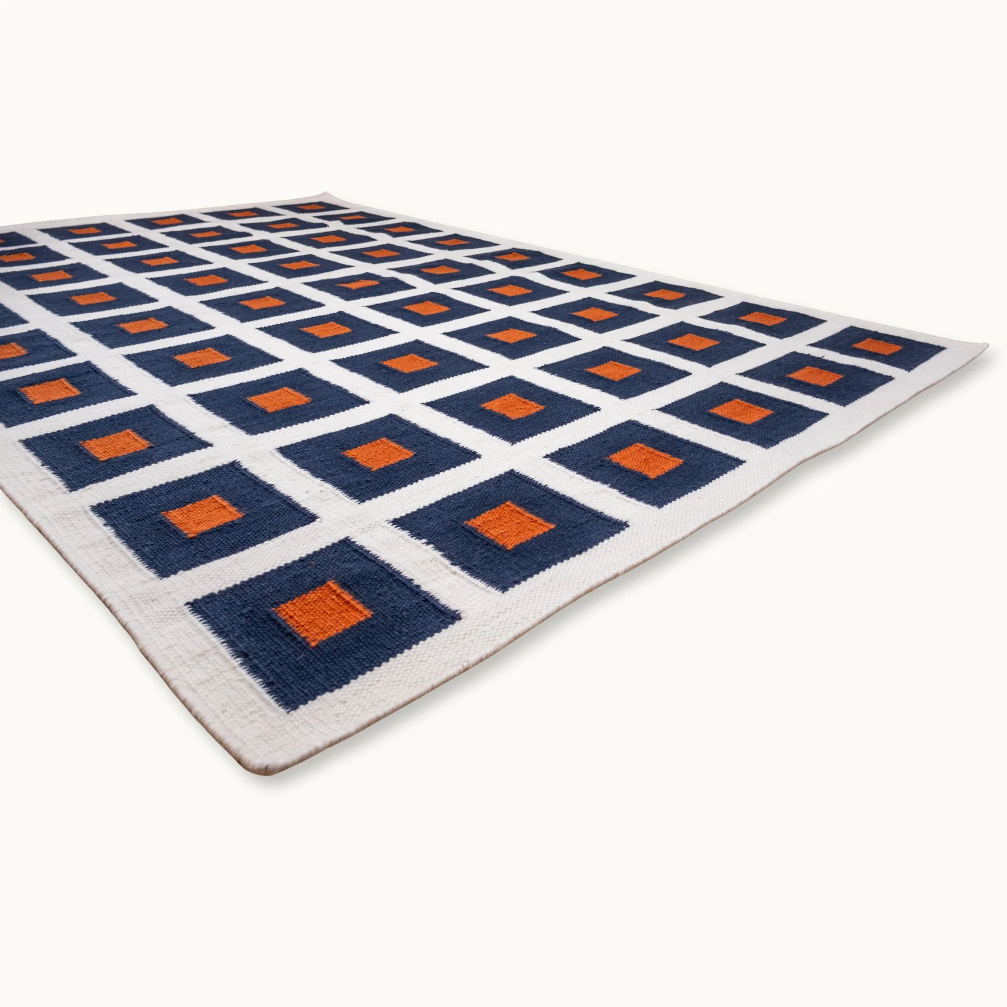 Handwoven wool flatweave rug with geometric square pattern in deep blue, whisper white, and Bombay brown tones.