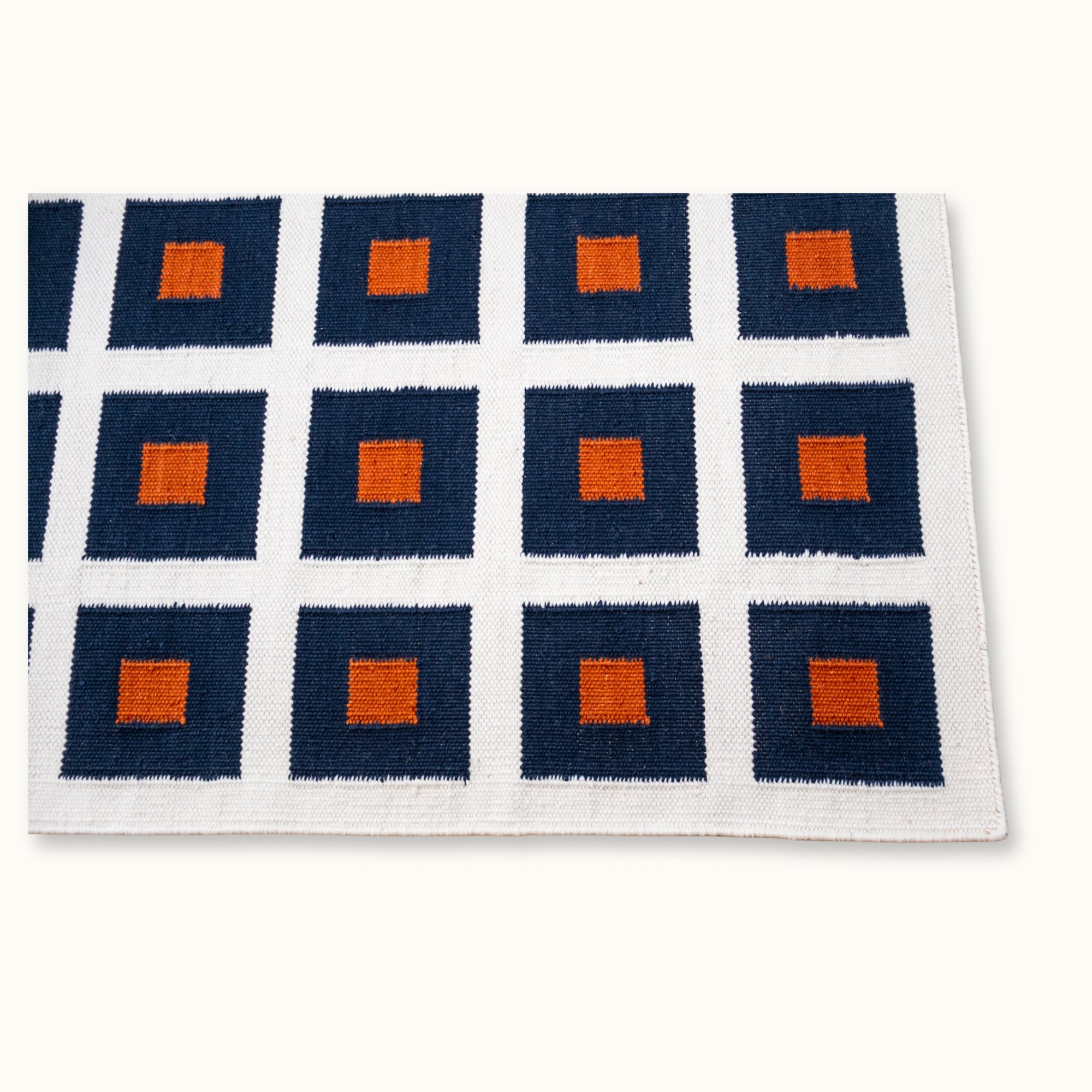 Handwoven wool flatweave rug with geometric square pattern in deep blue, whisper white, and Bombay brown tones.