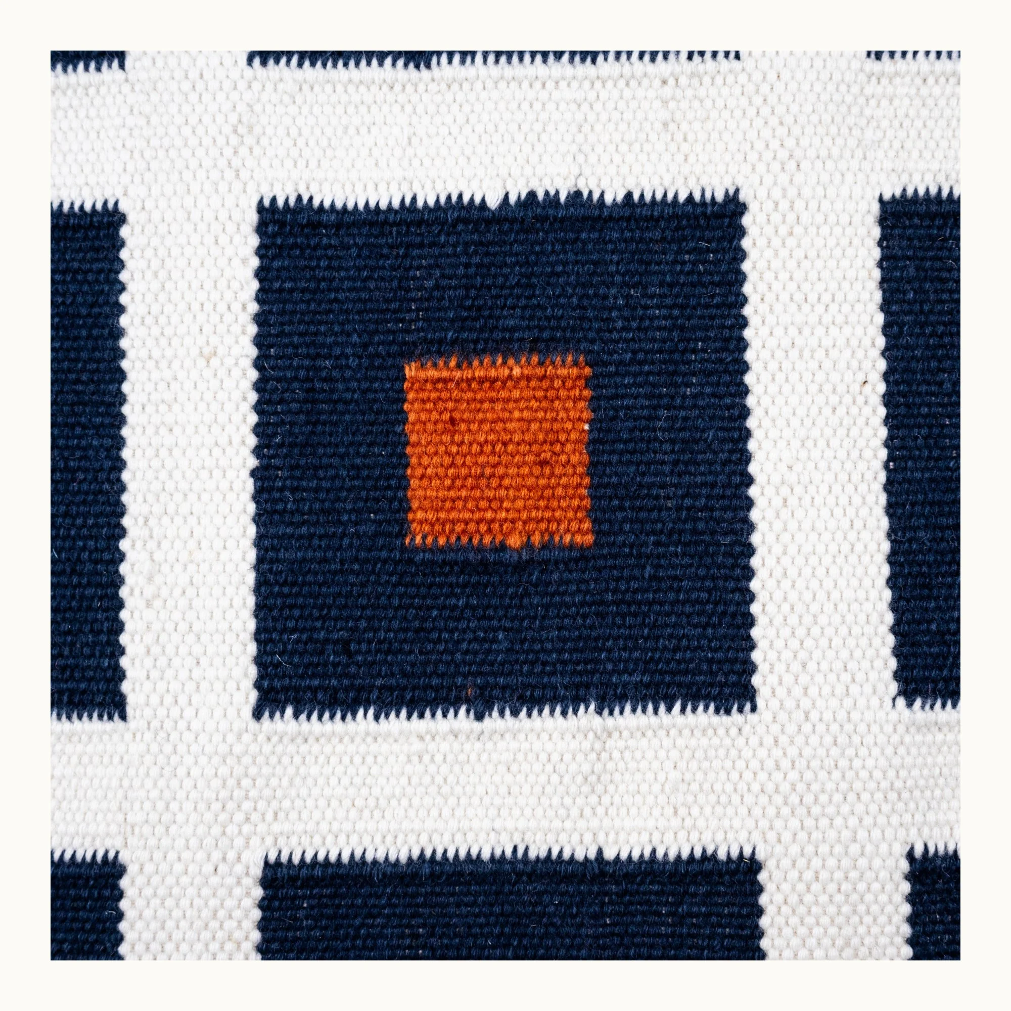 Handwoven wool flatweave rug with geometric square pattern in deep blue, whisper white, and Bombay brown tones.