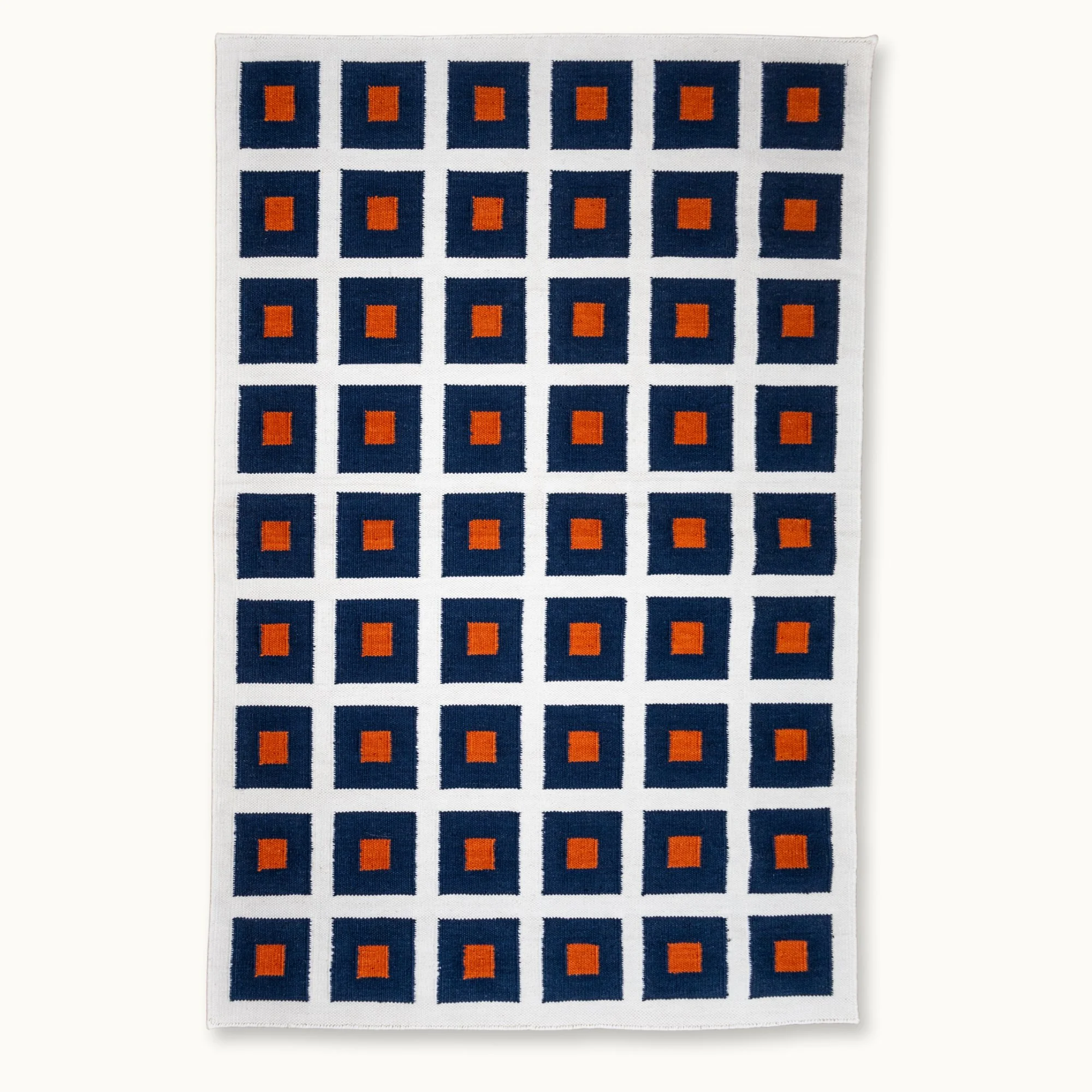 Handwoven wool flatweave rug with geometric square pattern in deep blue, whisper white, and Bombay brown tones.