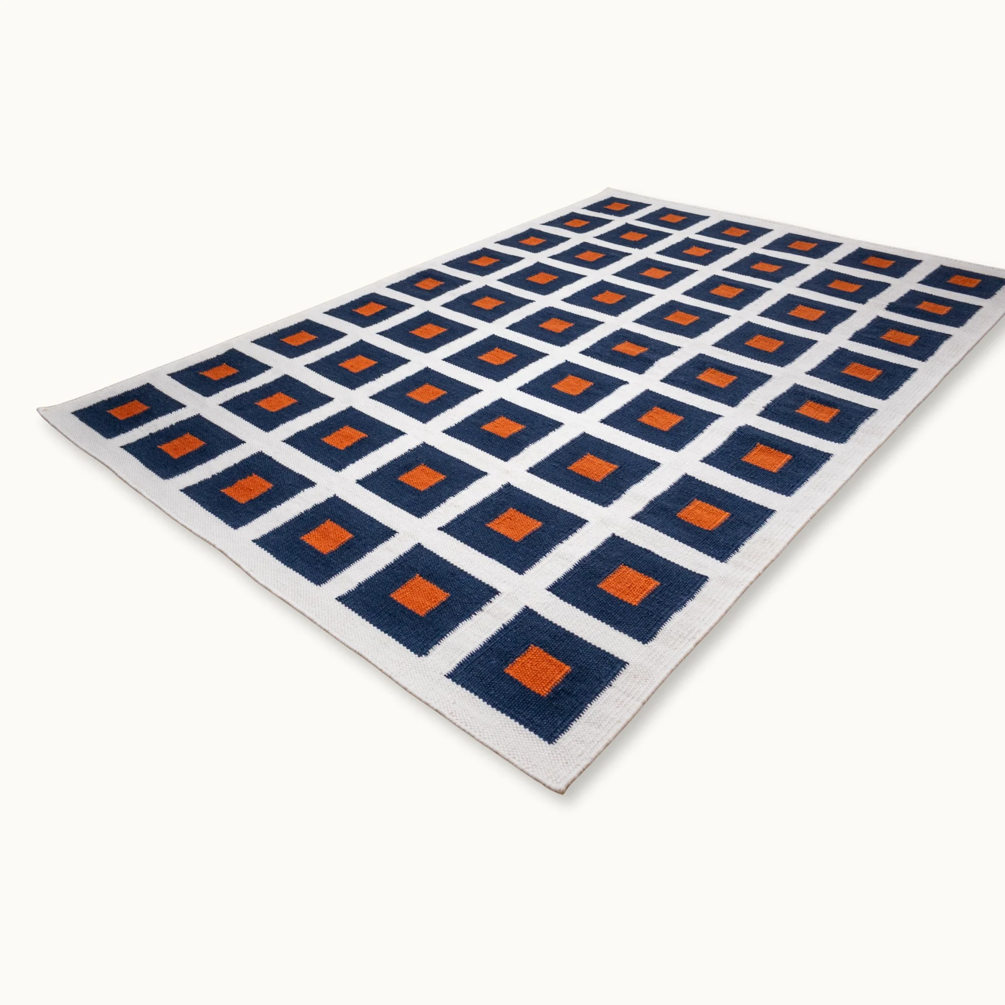 Handwoven wool flatweave rug with geometric square pattern in deep blue, whisper white, and Bombay brown tones.