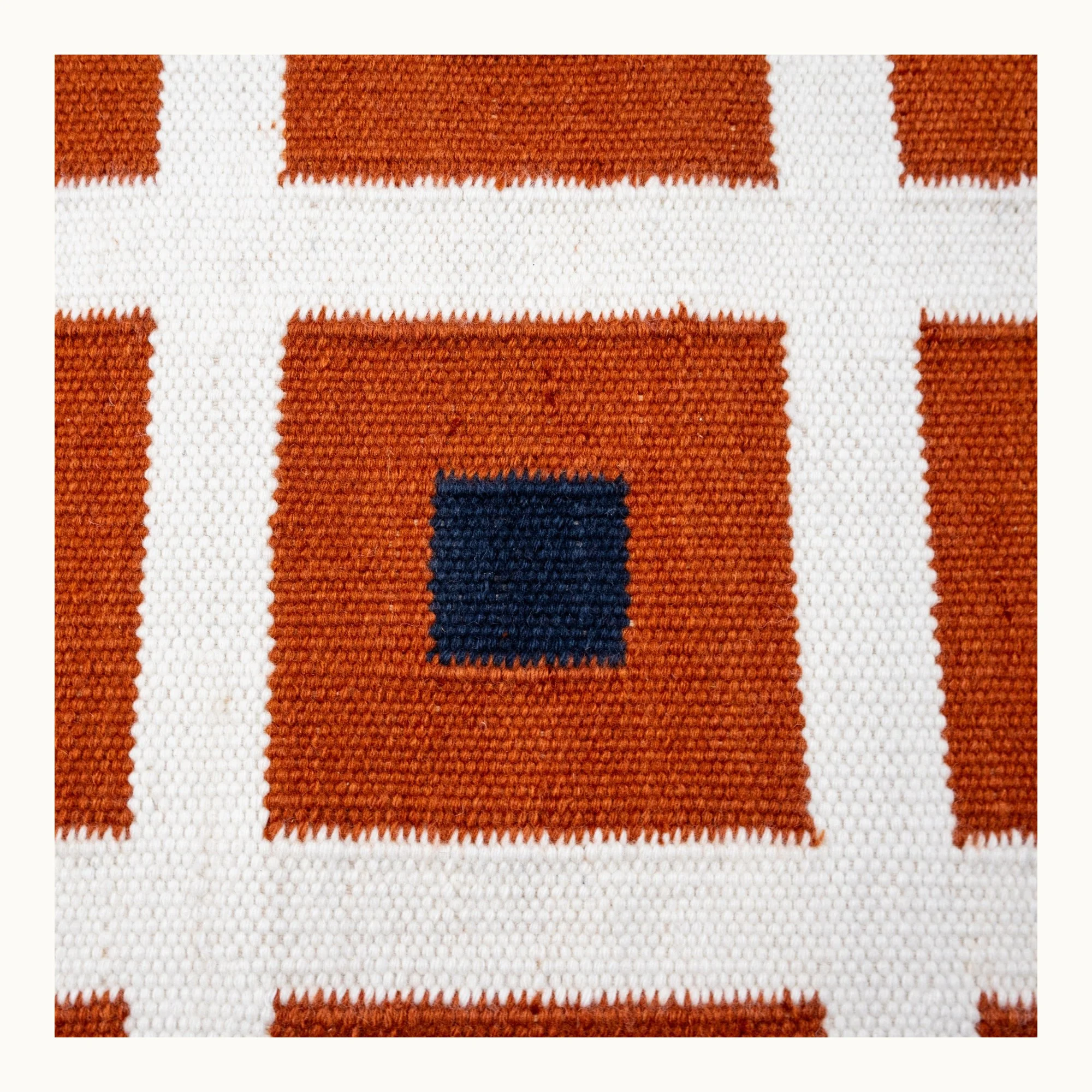 Handwoven wool flatweave rug with geometric square pattern in deep blue, whisper white, and Bombay brown tones.