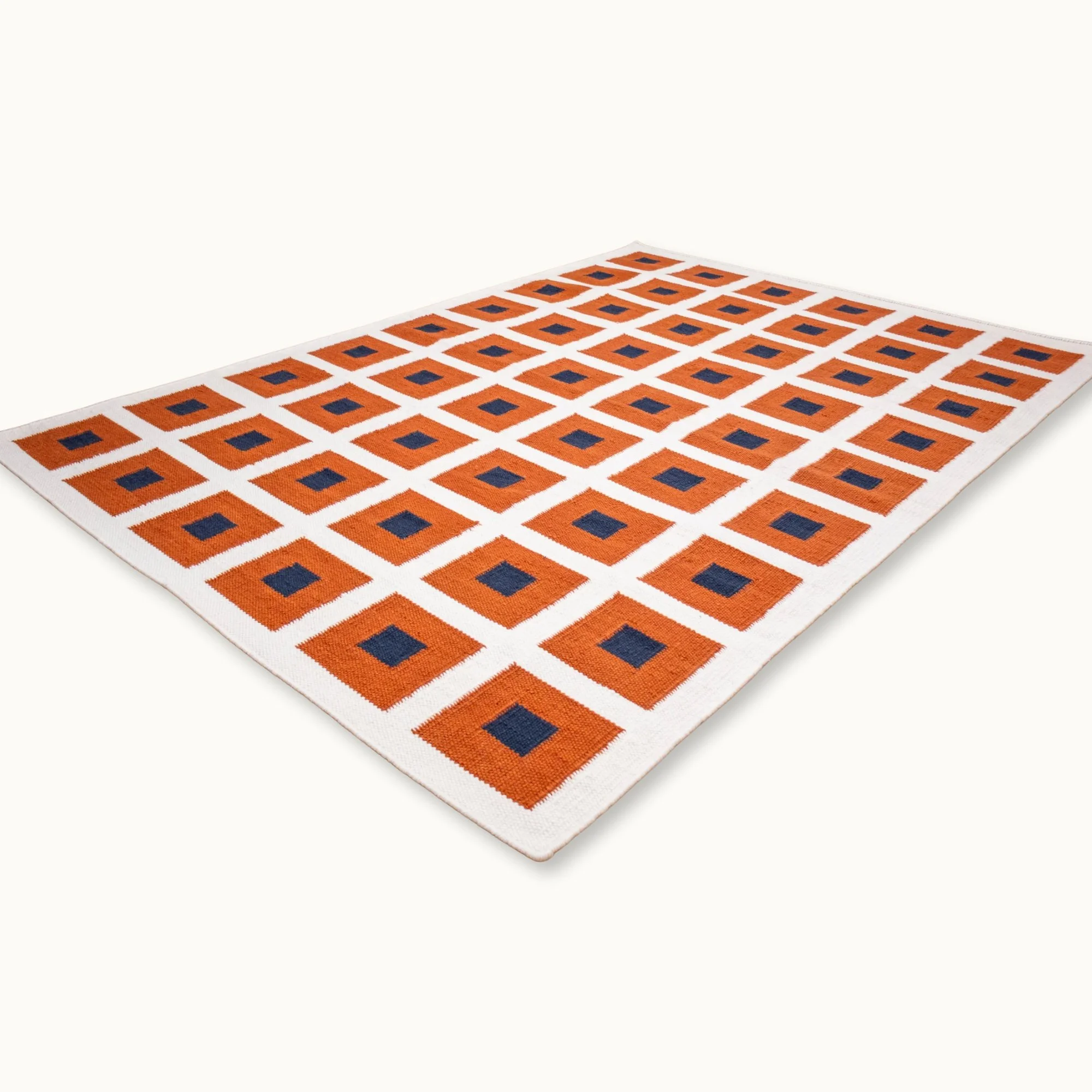 Handwoven wool flatweave rug with geometric square pattern in deep blue, whisper white, and Bombay brown tones.