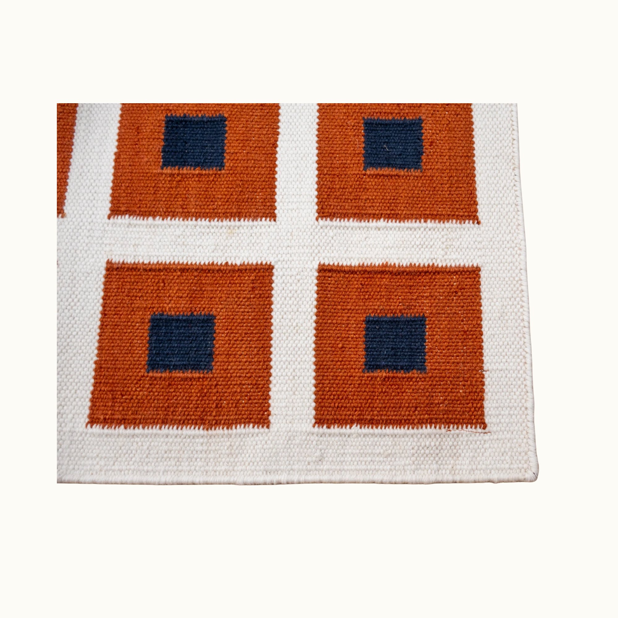 Handwoven wool flatweave rug with geometric square pattern in deep blue, whisper white, and Bombay brown tones.