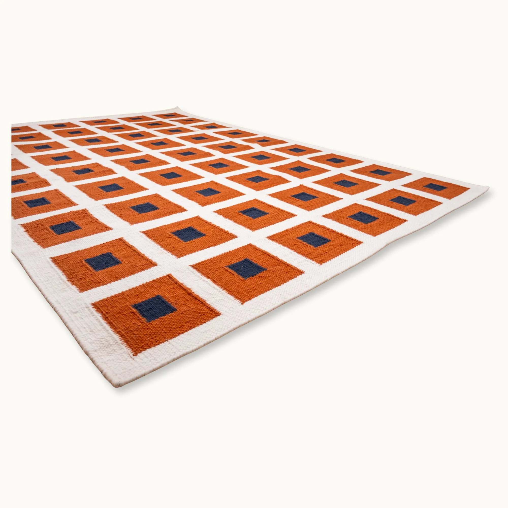 Handwoven wool flatweave rug with geometric square pattern in deep blue, whisper white, and Bombay brown tones.