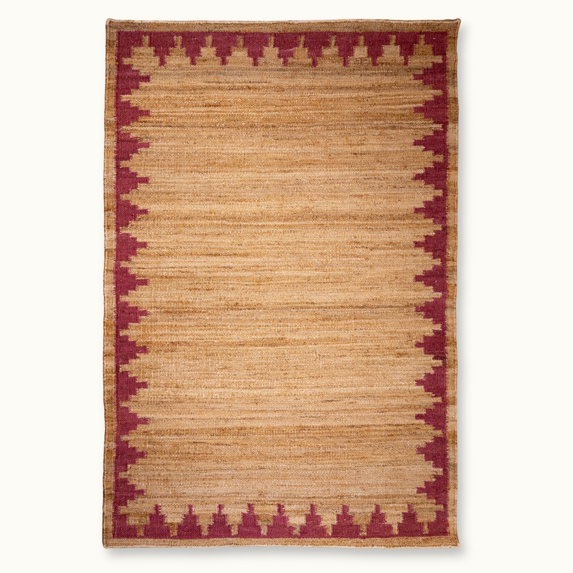 Handgeweven jute vloerkleed met een trapsgewijze geometrische rand in ingetogen roze en natuurlijke zandtinten.
