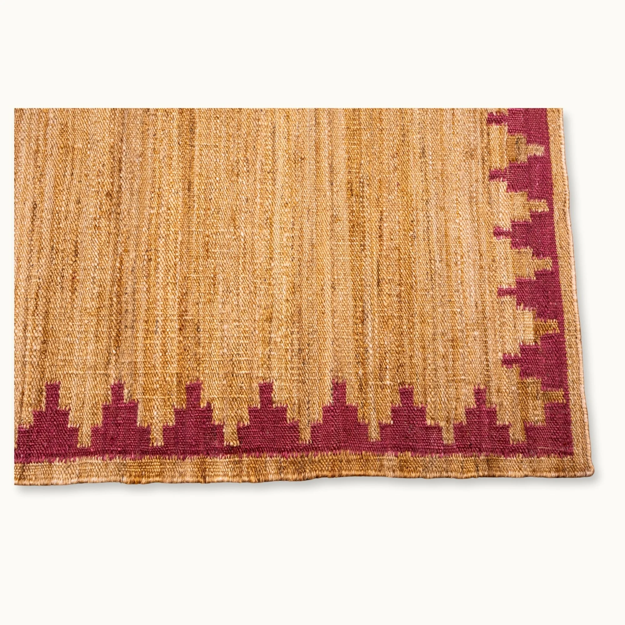 Handgeweven jute vloerkleed met een trapsgewijze geometrische rand in ingetogen roze en natuurlijke zandtinten.