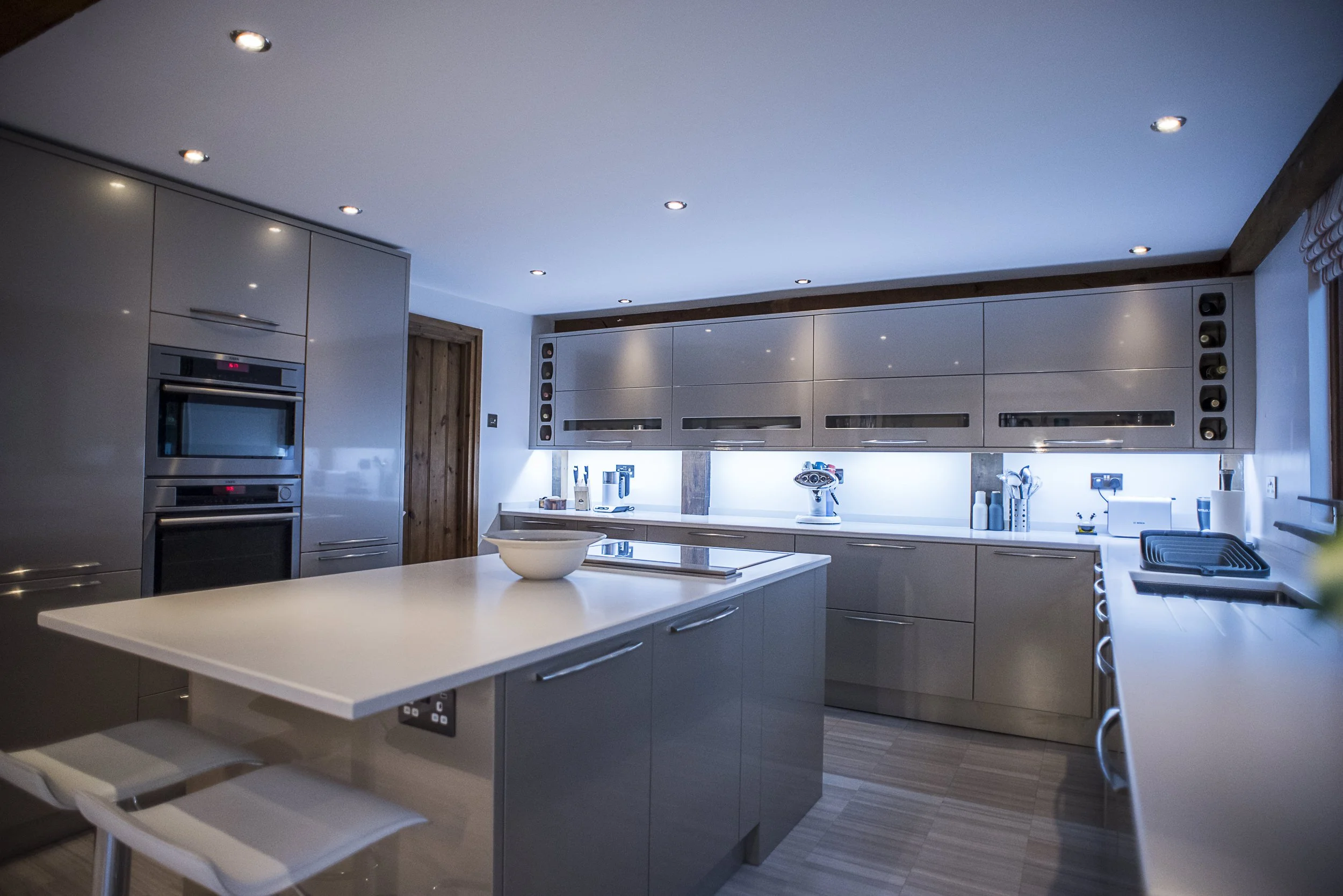 Modern kitchen with gray cabinets, white countertops, a kitchen island, built-in double oven, and kitchen appliances under a ceiling with recessed lighting.