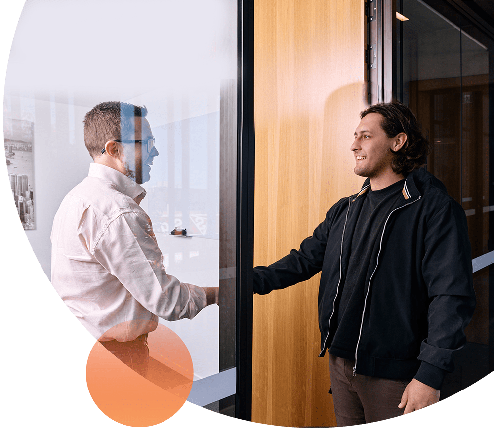 Financial advisor Peter Walters smiling with glasses and a white collared shirt, shaking hands with a client inside his office.