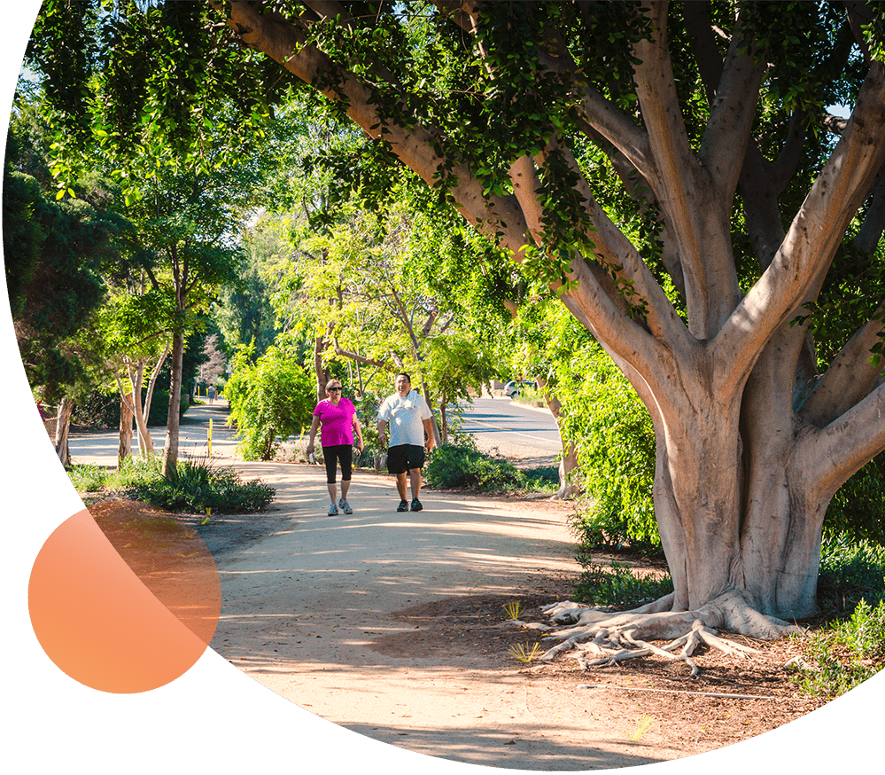 Two people walking in Queen's park, Toowoomba surrounded by trees and greenery.