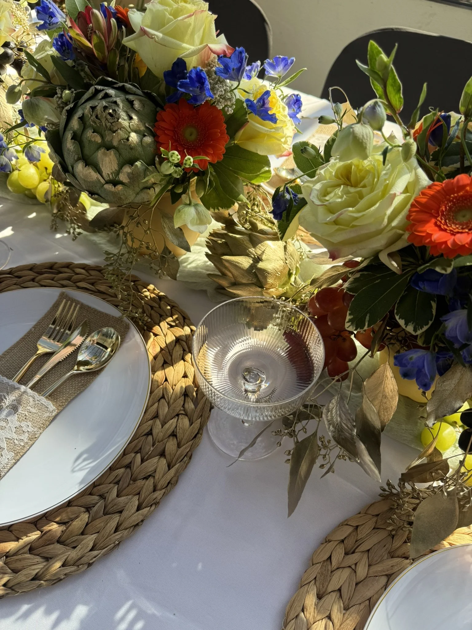 Elegant party centerpiece with roses, artichokes with gold tipped paint, red and orange gerbera daisies, brown charger plate and gold utensils available to rent in Monmouth County NJ  Central NJ - CelebrationShare
