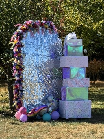 Arched party backdrop with glitter background, rainbow floral arrangements and six foot stacked gift display available to rent in Monmouth County NJ - CelebrationShare