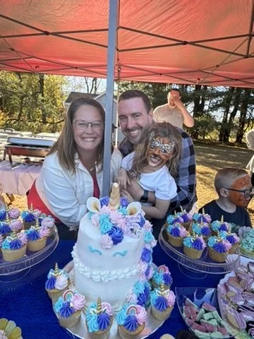 Family celebrating fifth birthday party under tent with purple and pink unicorn cake and cupcakes at outdoor farm birthday in Millstone Township Monmouth County NJ Central Jersey - CelebrationShare