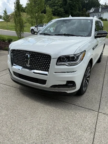 White SUV parked on a driveway with trees and houses in the background.