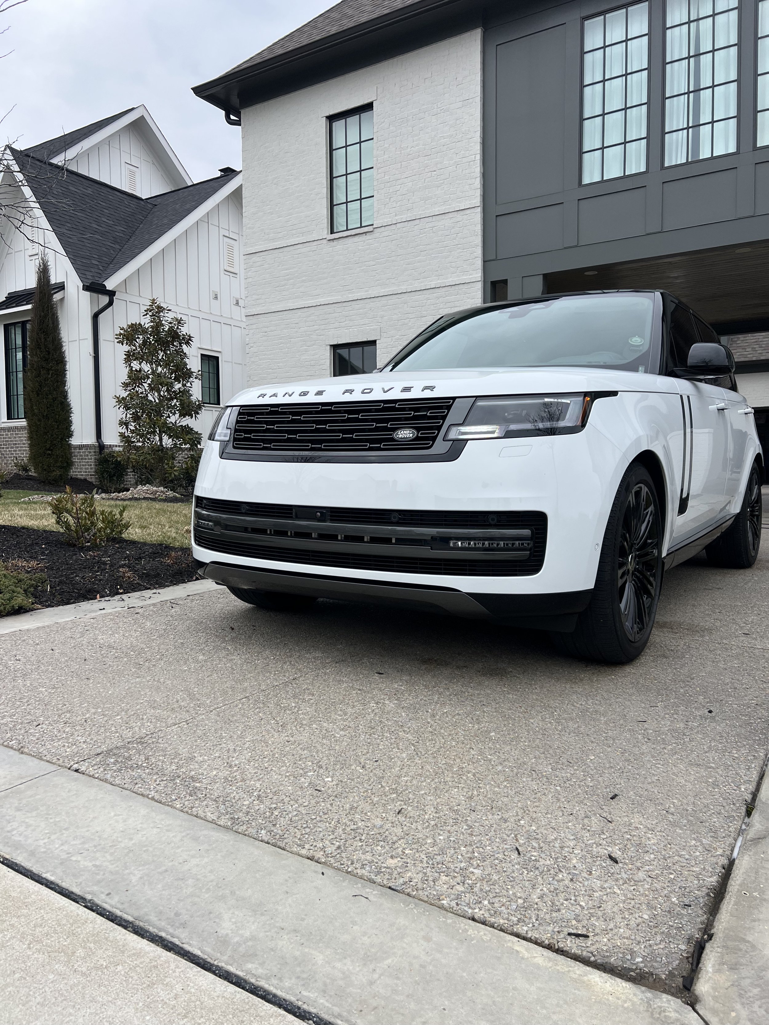 White Range Rover parked in driveway outside modern house with white and gray exterior walls.