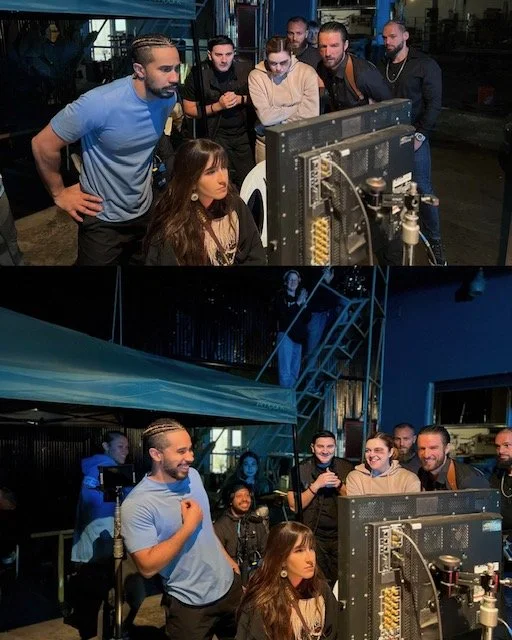 Group of people watching a woman at a computer screen in a film or television studio, with some smiling and one woman looking serious.