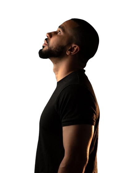 Side profile of a man with a beard wearing a black t-shirt and cap, looking upward against a black background.