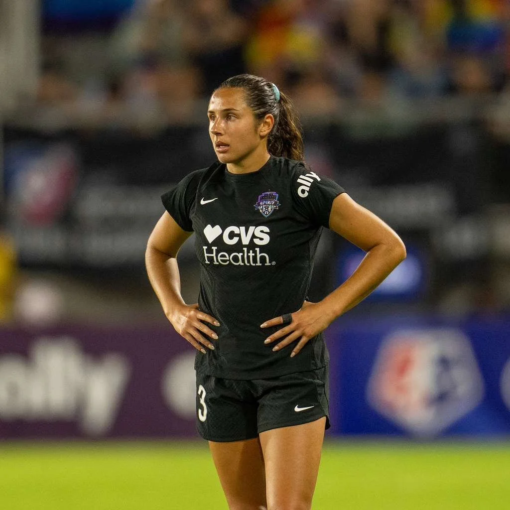 A female soccer player standing on the field with hands on her hips, wearing a black jersey with the number 3, along with black shorts, during a match.