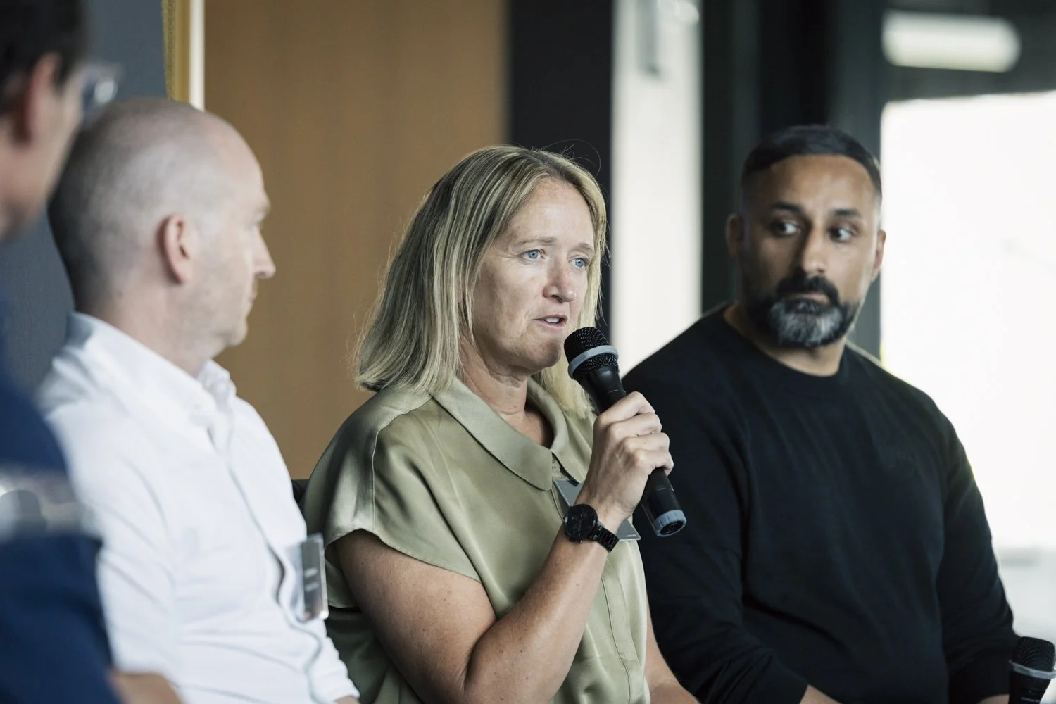 Dawn Scott speaking into a microphone during a panel discussion, with three other people sitting beside her and listening.