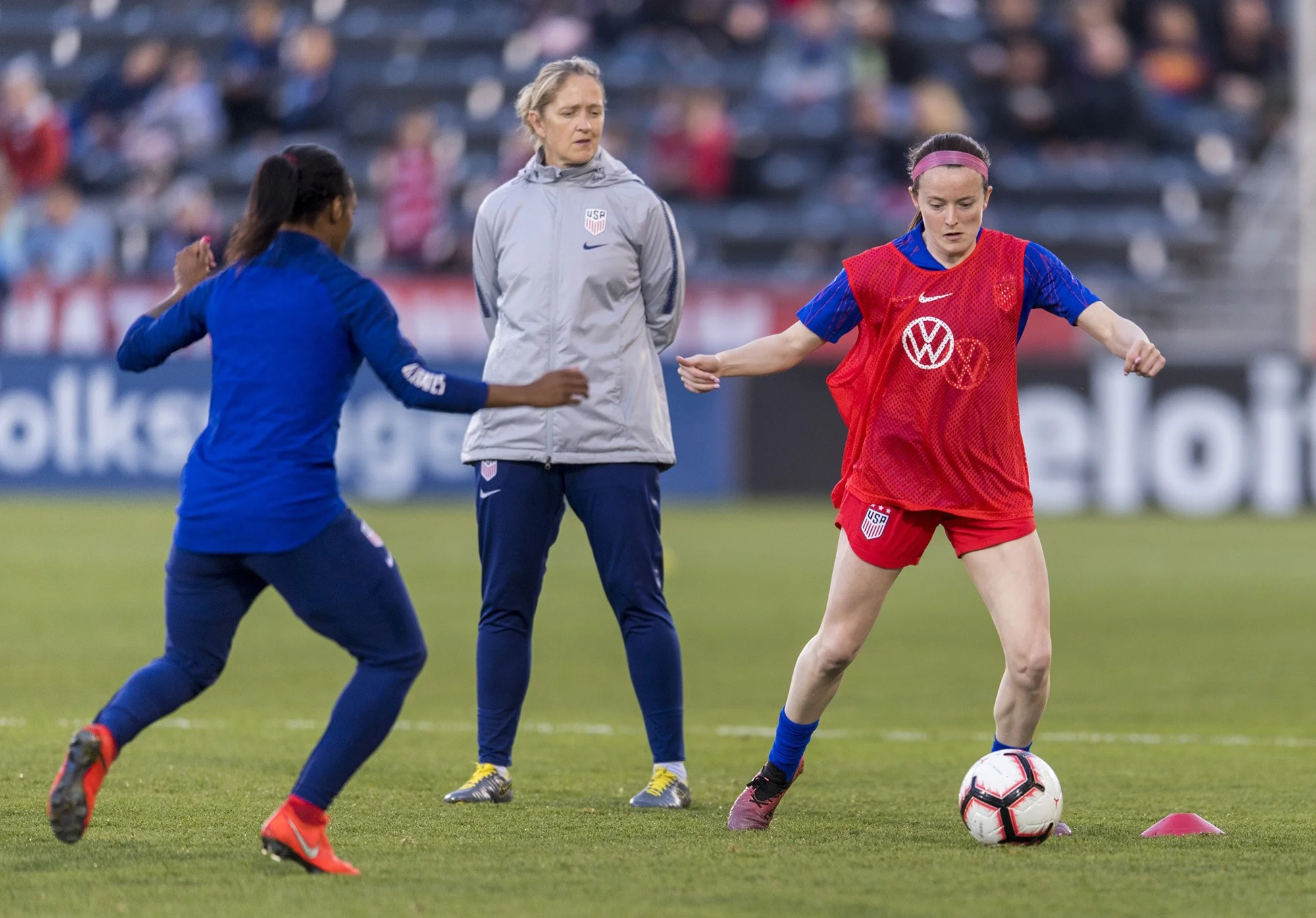Women soccer players practicing on the field with a coach watching.