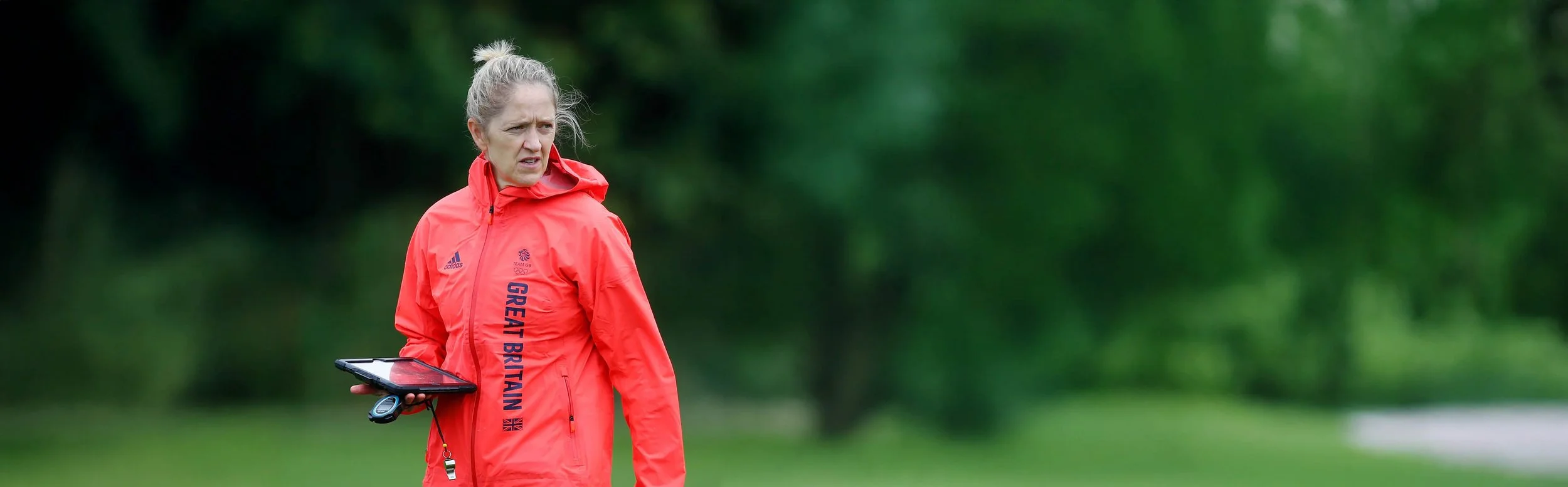 Dawn Scott, standing outdoors with green trees in the background.