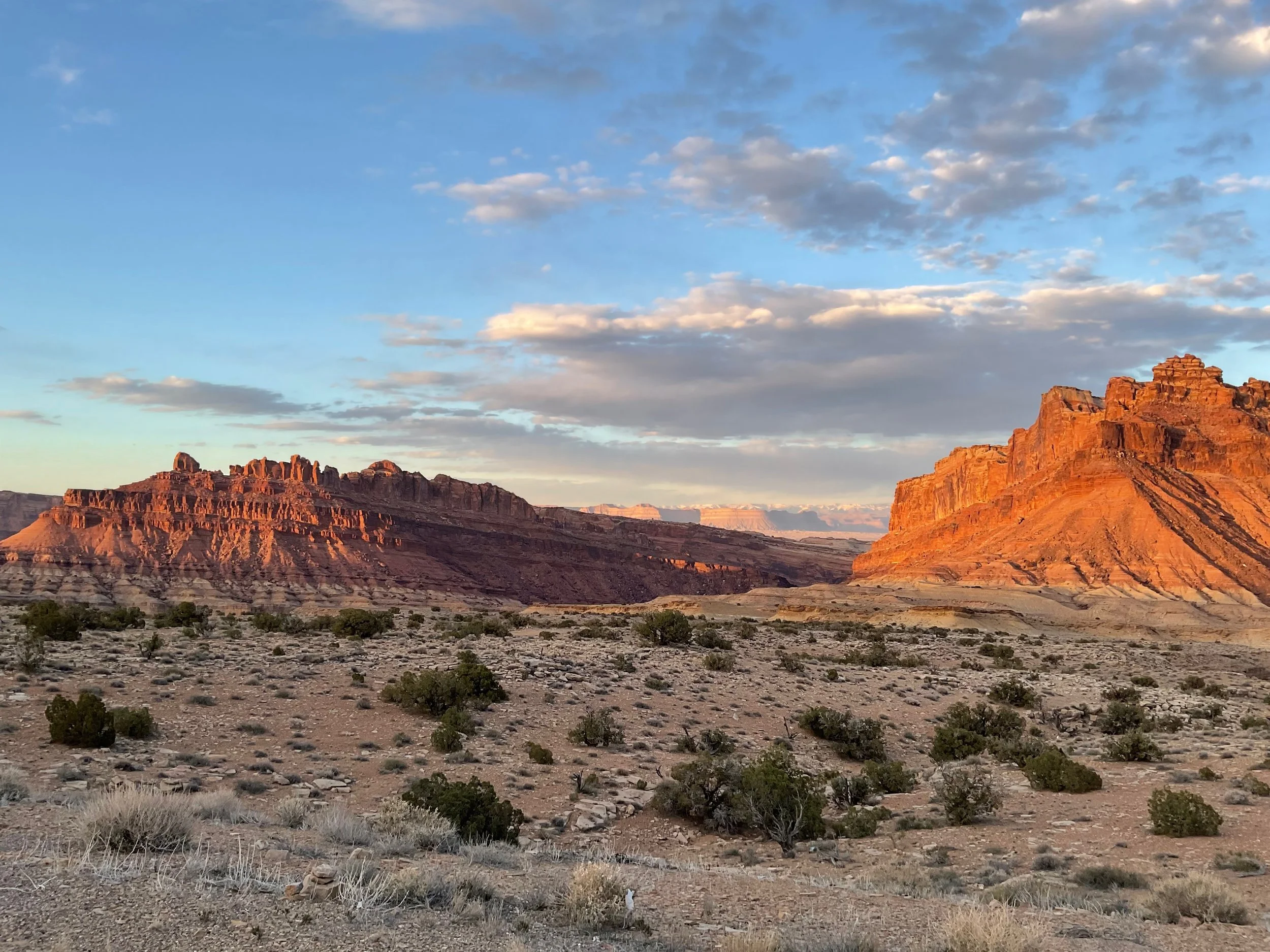 Sunset over arid desert landscape with layered red rock formations and sparse vegetation
