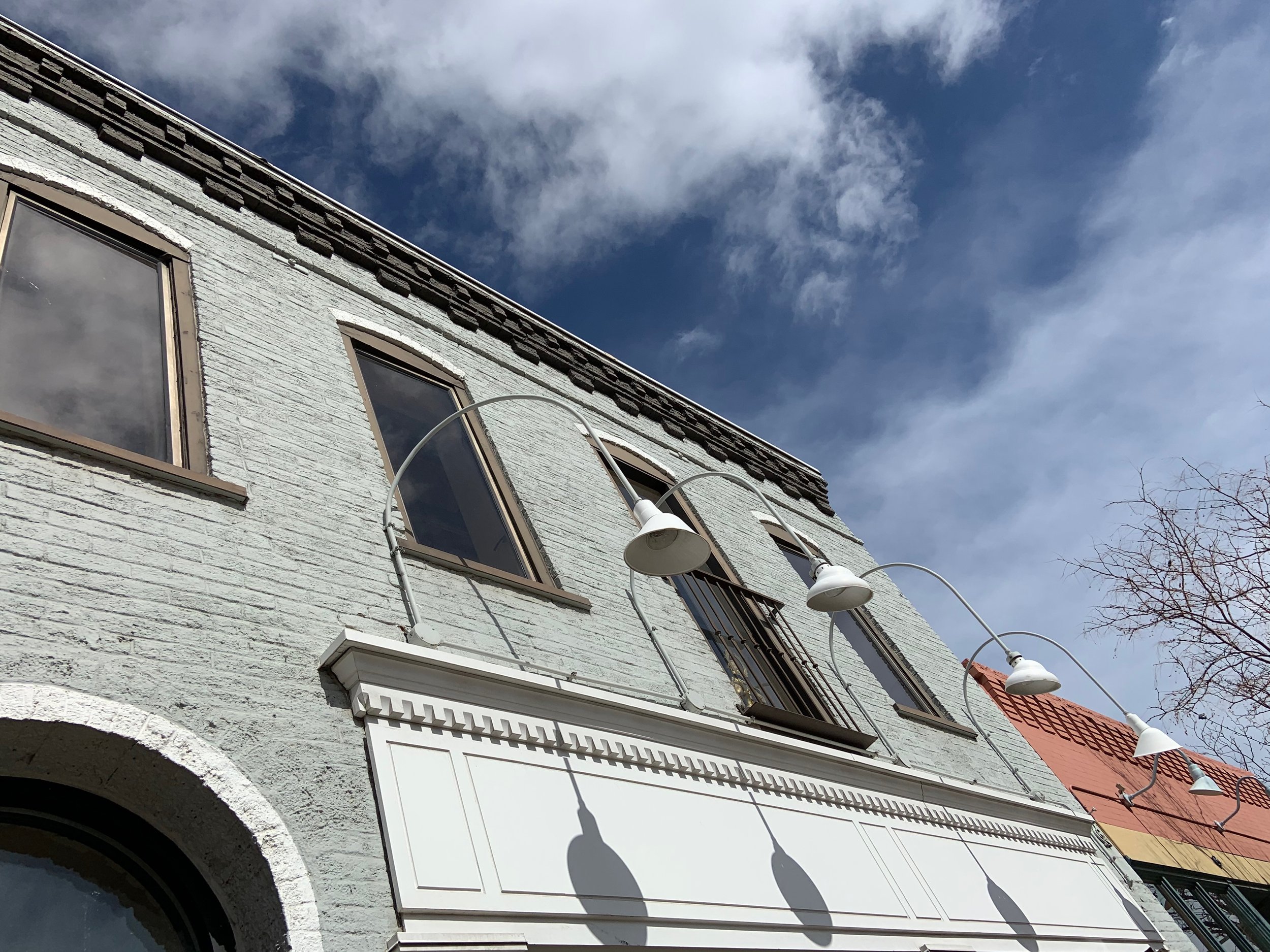Upside-down view of a white brick building with large windows, outdoor wall lights, and a partly cloudy sky.