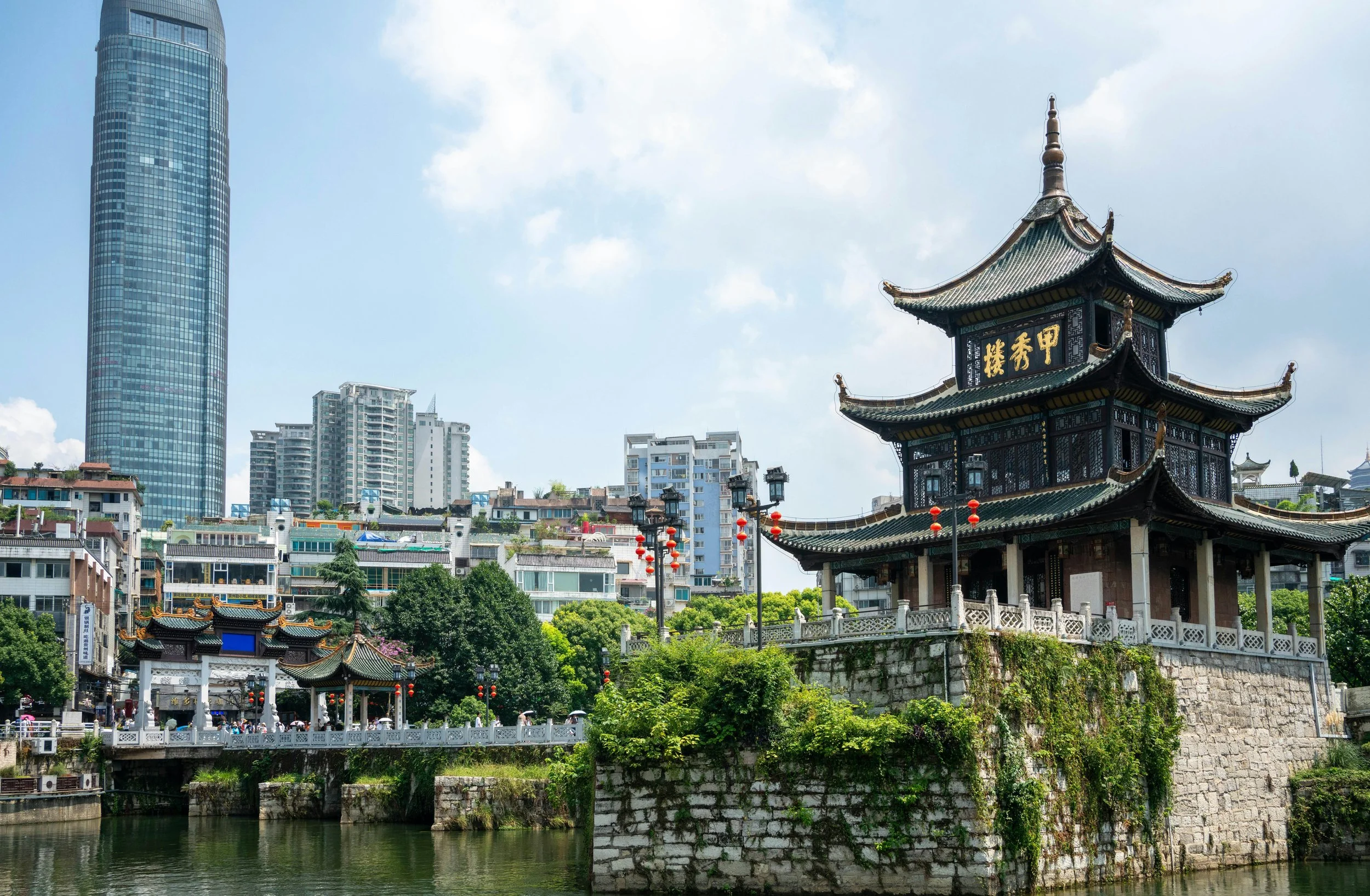 Traditionelles chinesisches Pavillon vor modernen Hochhäusern, umgeben von Bäumen, vor blauem Himmel. Eine Szene aus Guiyang, Guizhou in Südchina.